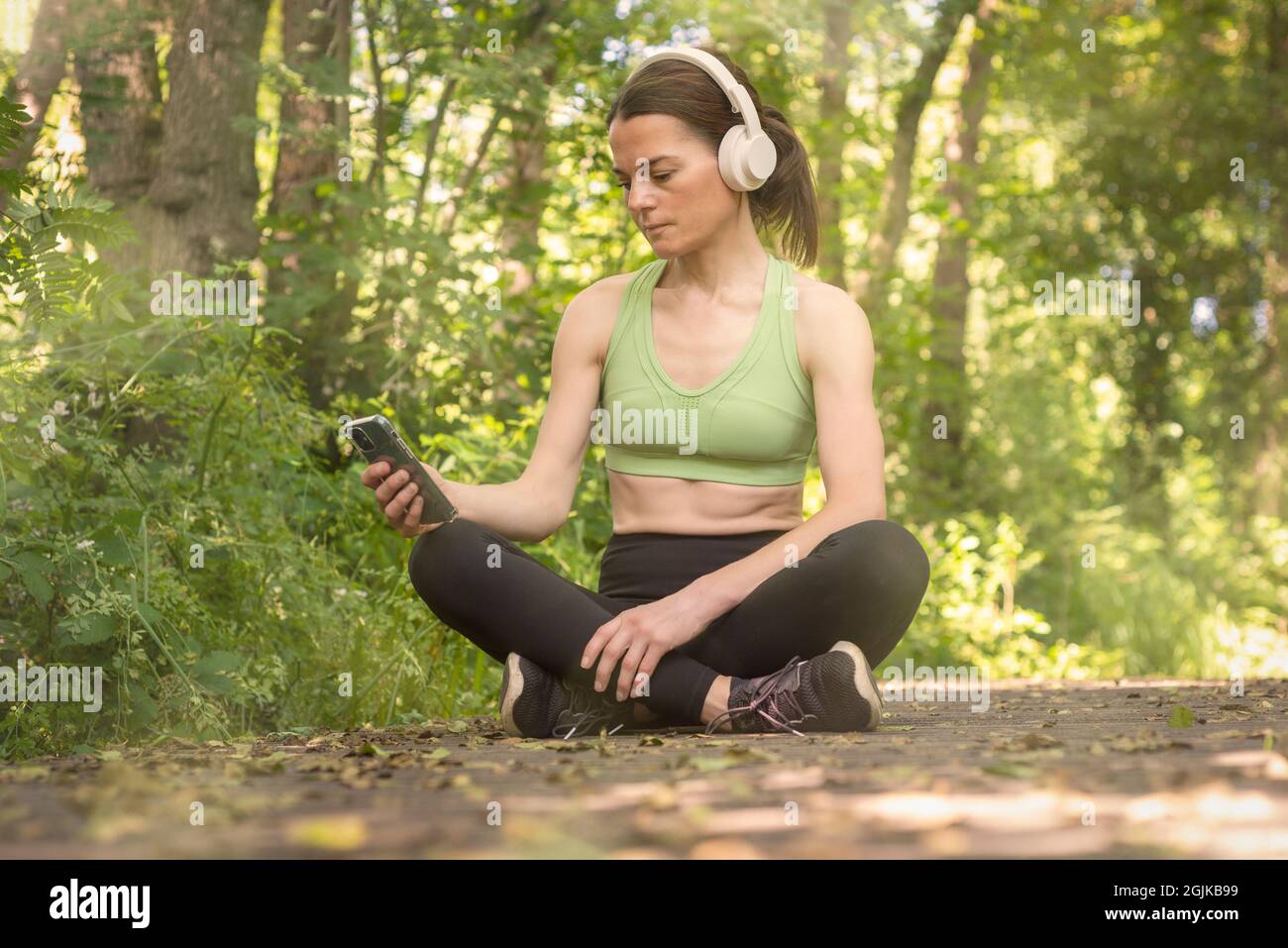 Sportliche Frau, die im aktiven Sitzen sitzt und Musik über Kopfhörer hört. Headspace. Stockfoto