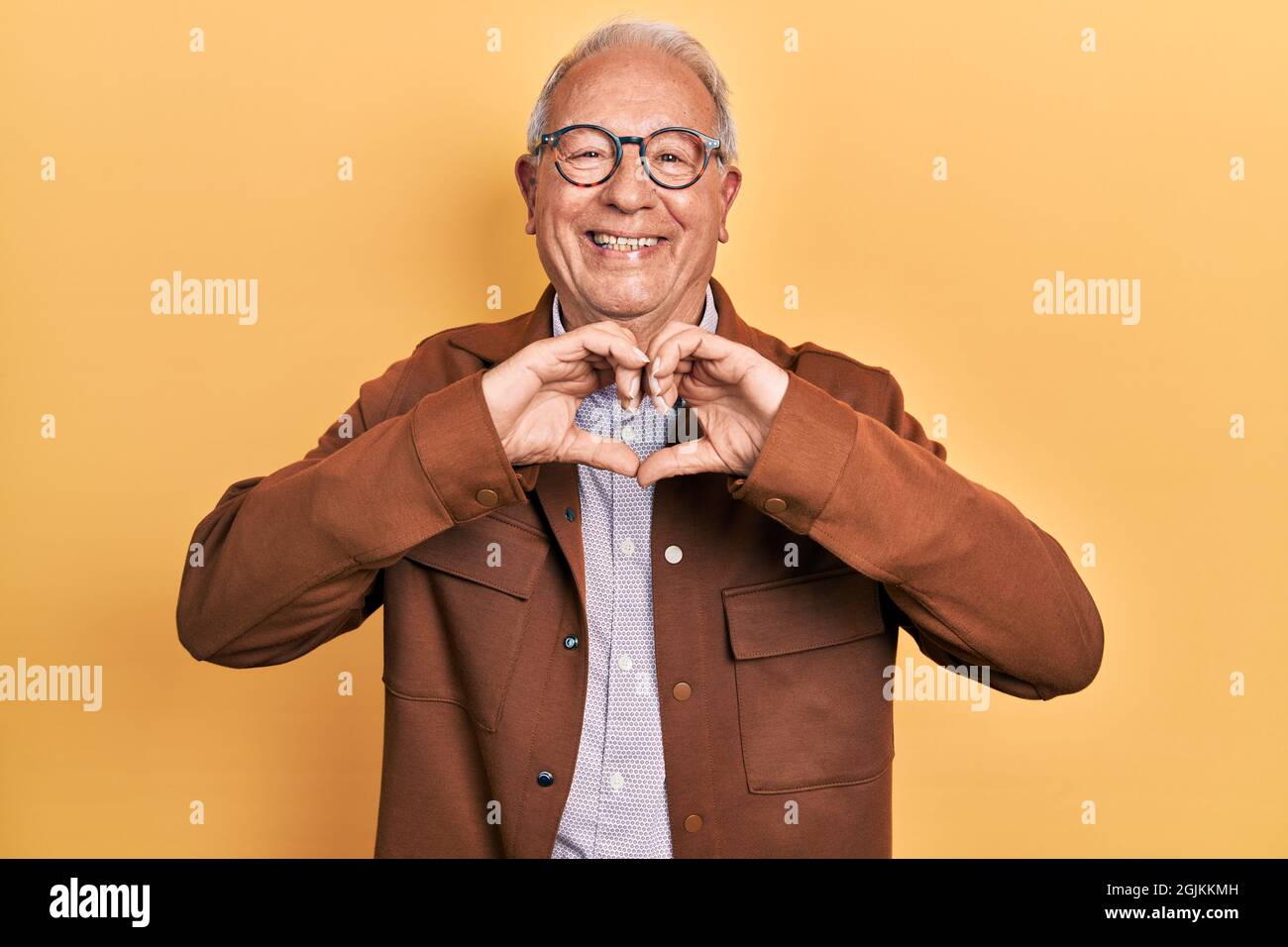 Senior Mann mit grauen Haaren trägt Casual Jacke und Brille lächelnd in der Liebe tun Herz Symbol Form mit Händen. Romantisches Konzept. Stockfoto