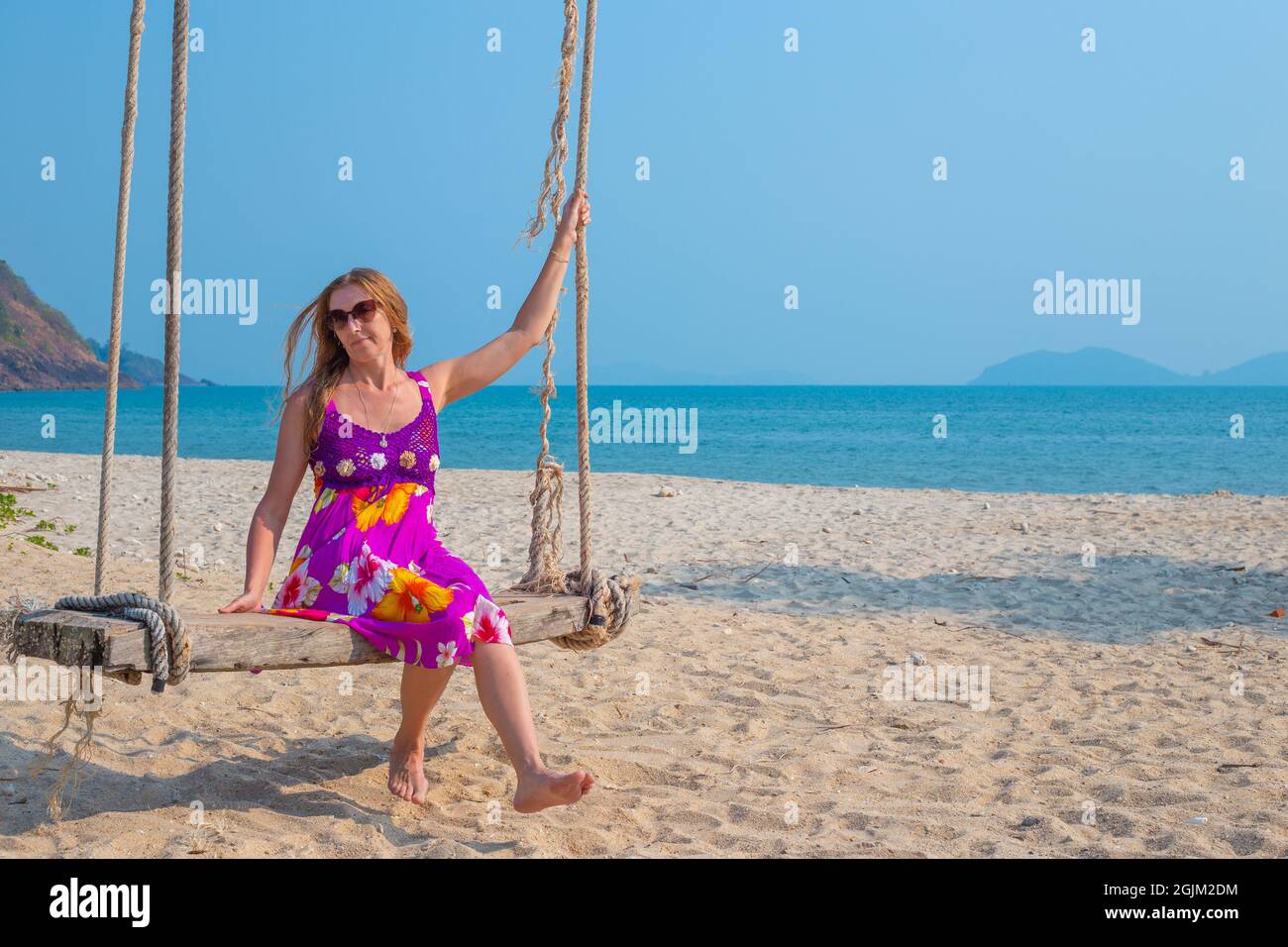 Junge Frau schwingt auf einer Schaukel, die an einer Palme am Meer hängt. Reisen und Tourismus in die tropischen Länder Asiens. Stockfoto