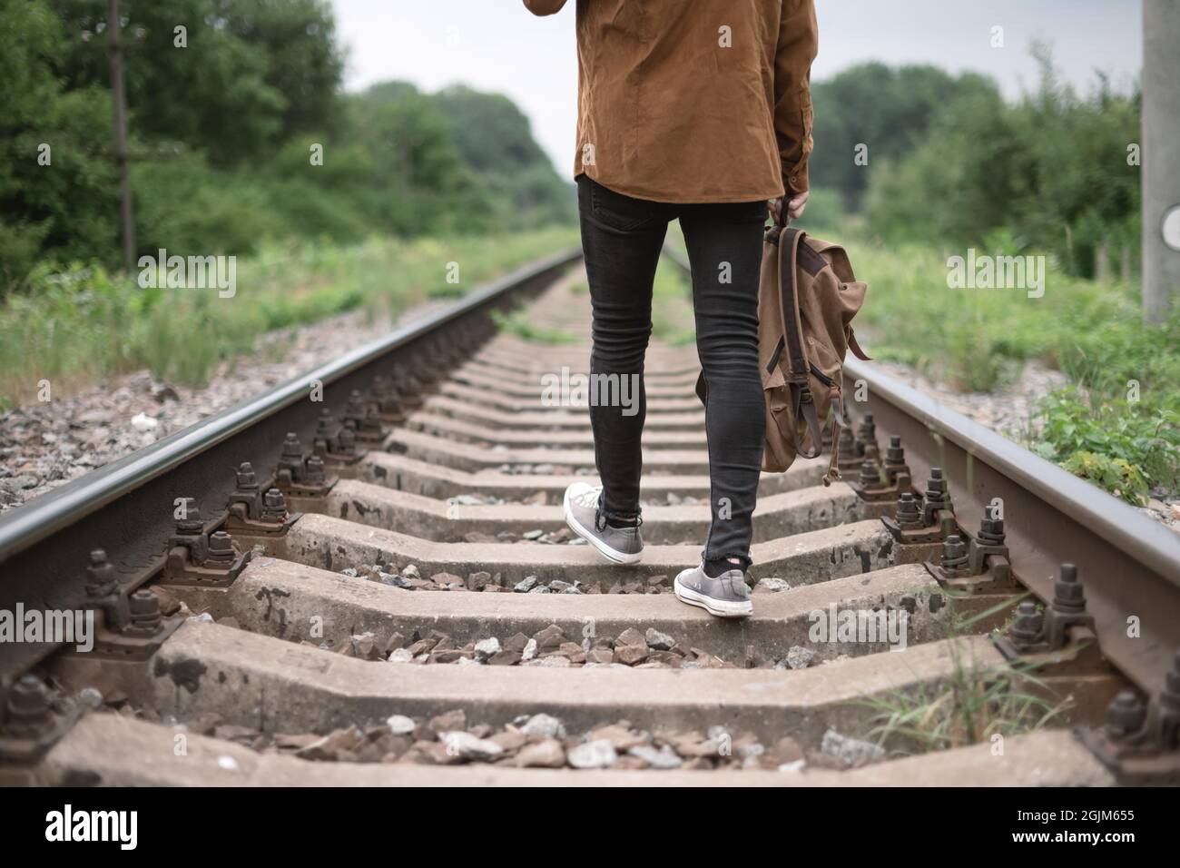 Hipster Teen in schwarzer Jeans-Hose und grauen Sneakers mit Rucksack auf der Eisenbahn. Reisekonzept Stockfoto