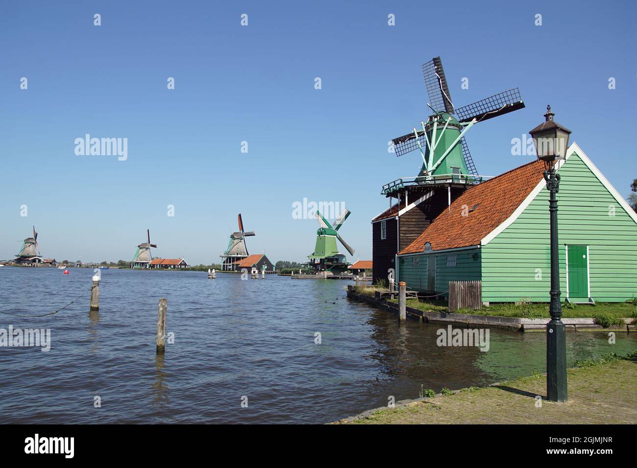 Würzige Windmühle De Huisman im Lager De Haan am Fluss De Zaan, Windmühlen in der Ferne von Zaanse Schans, einem holländischen Freilichtmuseum. Stockfoto