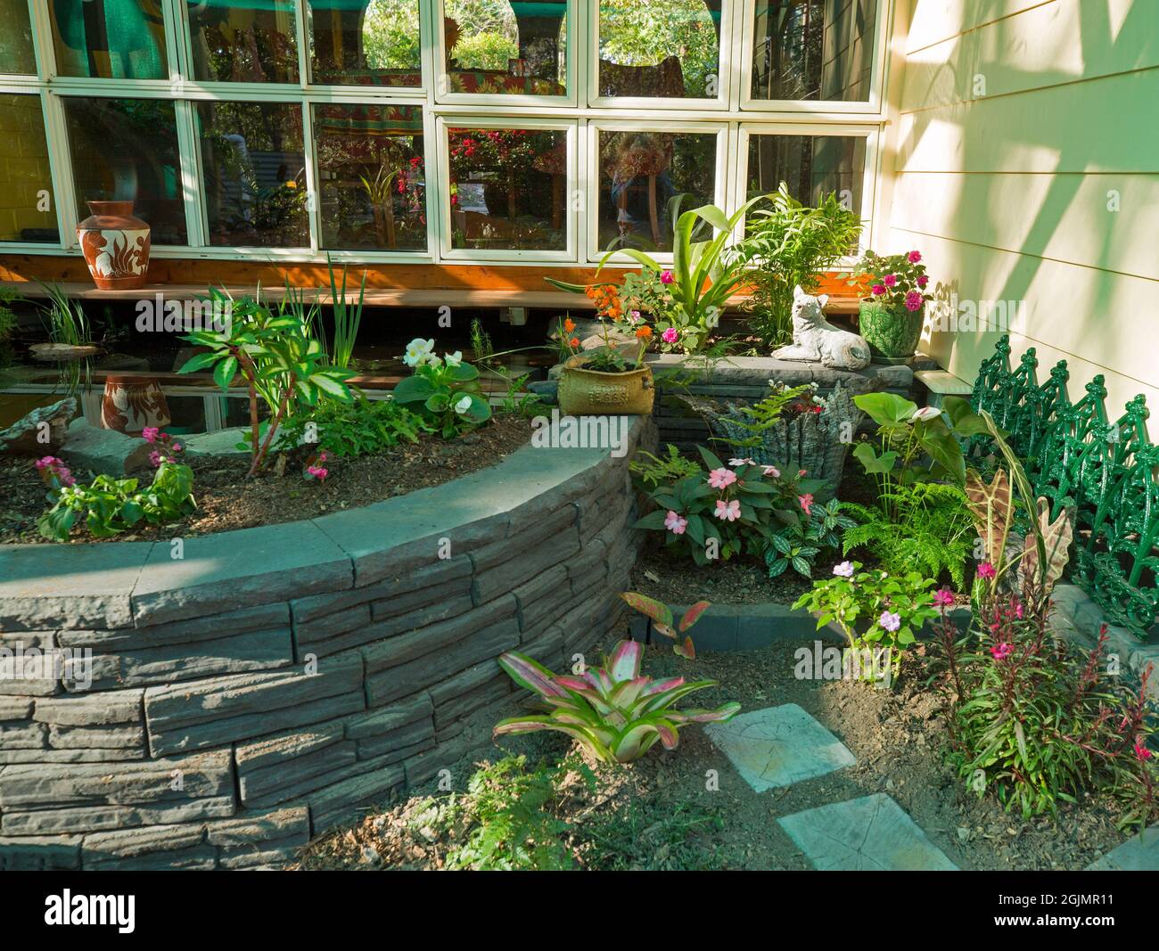 Neu angelegter Innenhofgarten mit gebogener Ziegelmauer von angehobenen Blumenbeet-Höhen und jungen Pflanzen, die neben Fenstern der Terrasse wachsen Stockfoto