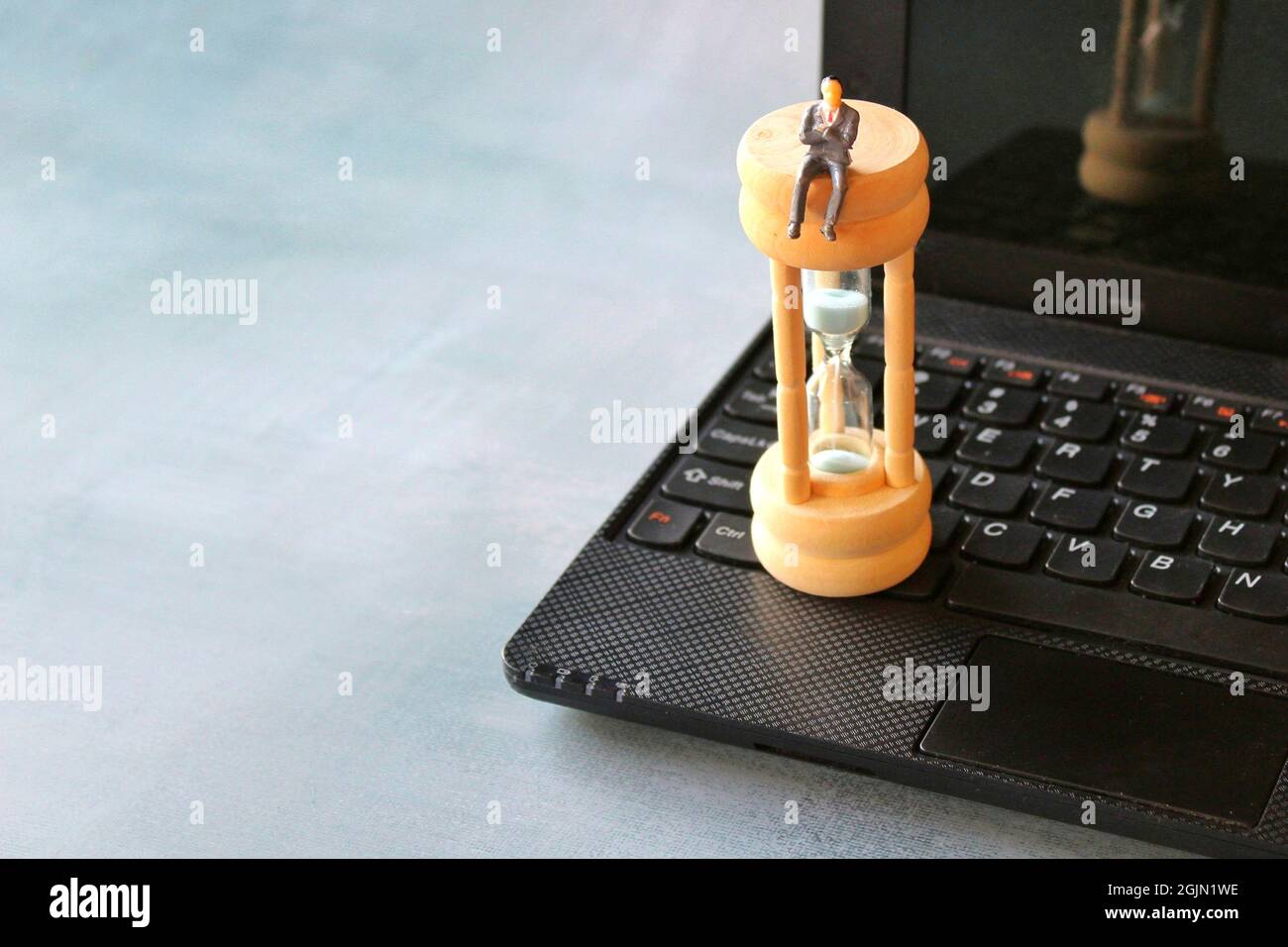 Miniaturunternehmer sitzen auf Sanduhr und Laptop. Konzept für Zeitmanagement und Countdown bis zum Stichtag Stockfoto