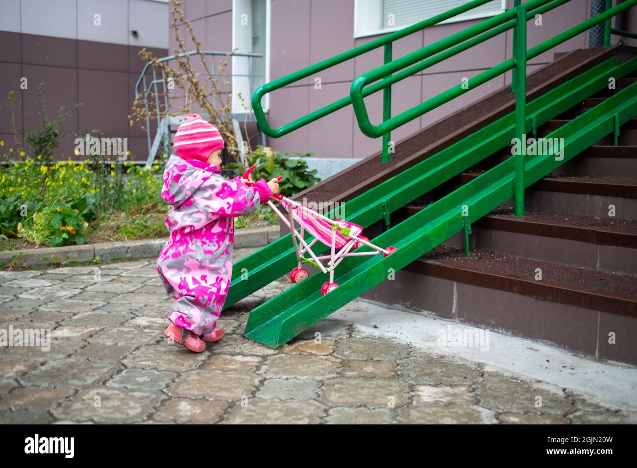 Nettes Kleinkind schleppt einen Spielzeug-Kinderwagen entlang der Rampe der  Treppe. Hangwanderweg für behinderte Menschen, Personen, die Kinderwagen  schieben, Wagen mit Edelstahlstangen Stockfotografie - Alamy