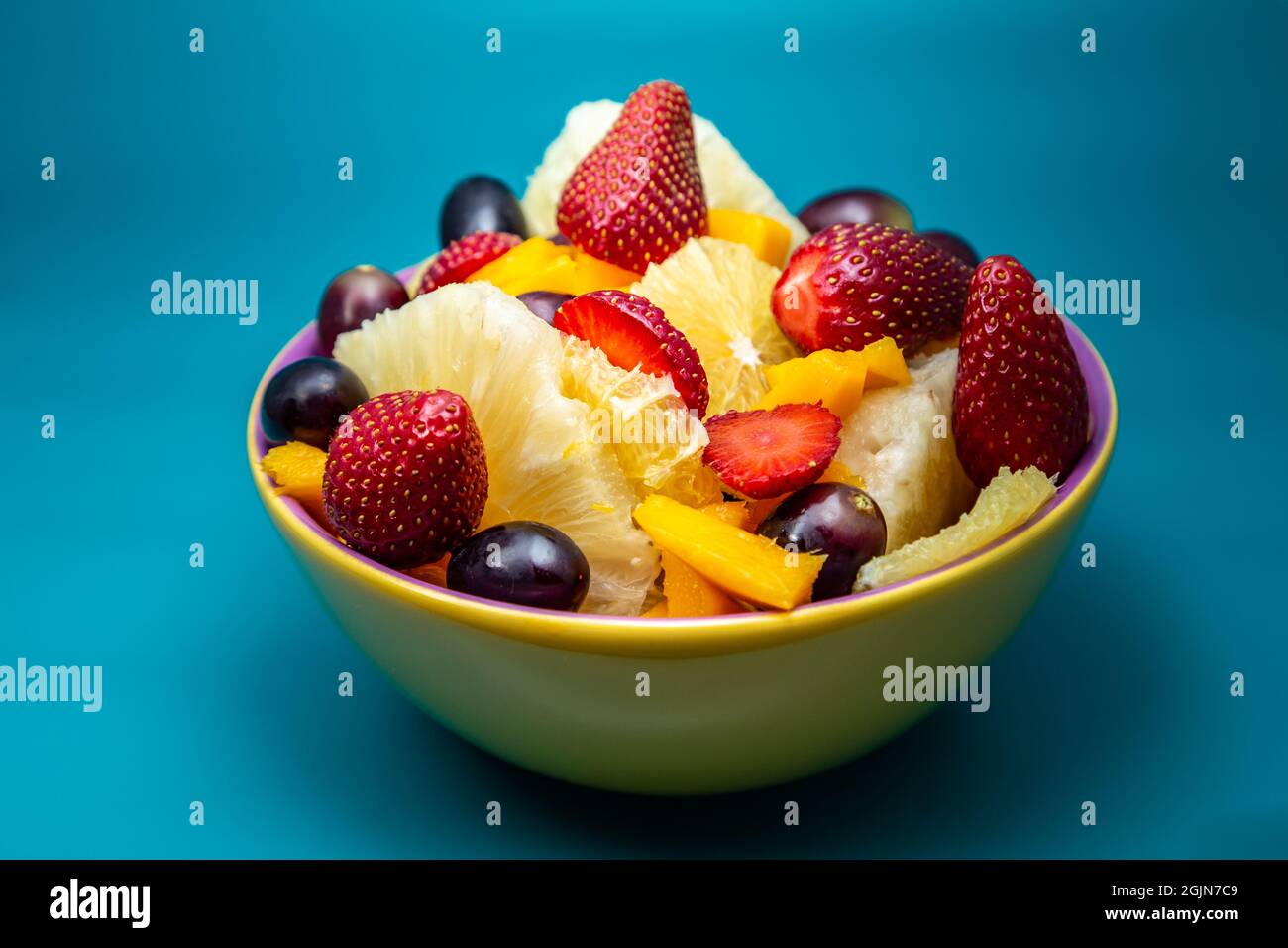 Eine Portion Obstsalat in einer gelben Schüssel mit tiffany-blauem Hintergrund. Stockfoto