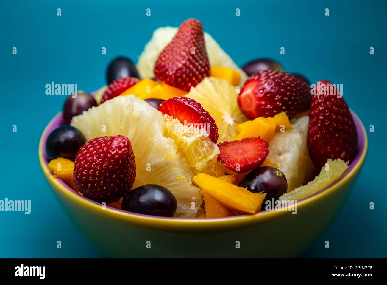 Eine Portion Obstsalat in einer gelben Schüssel mit tiffany-blauem Hintergrund. Stockfoto