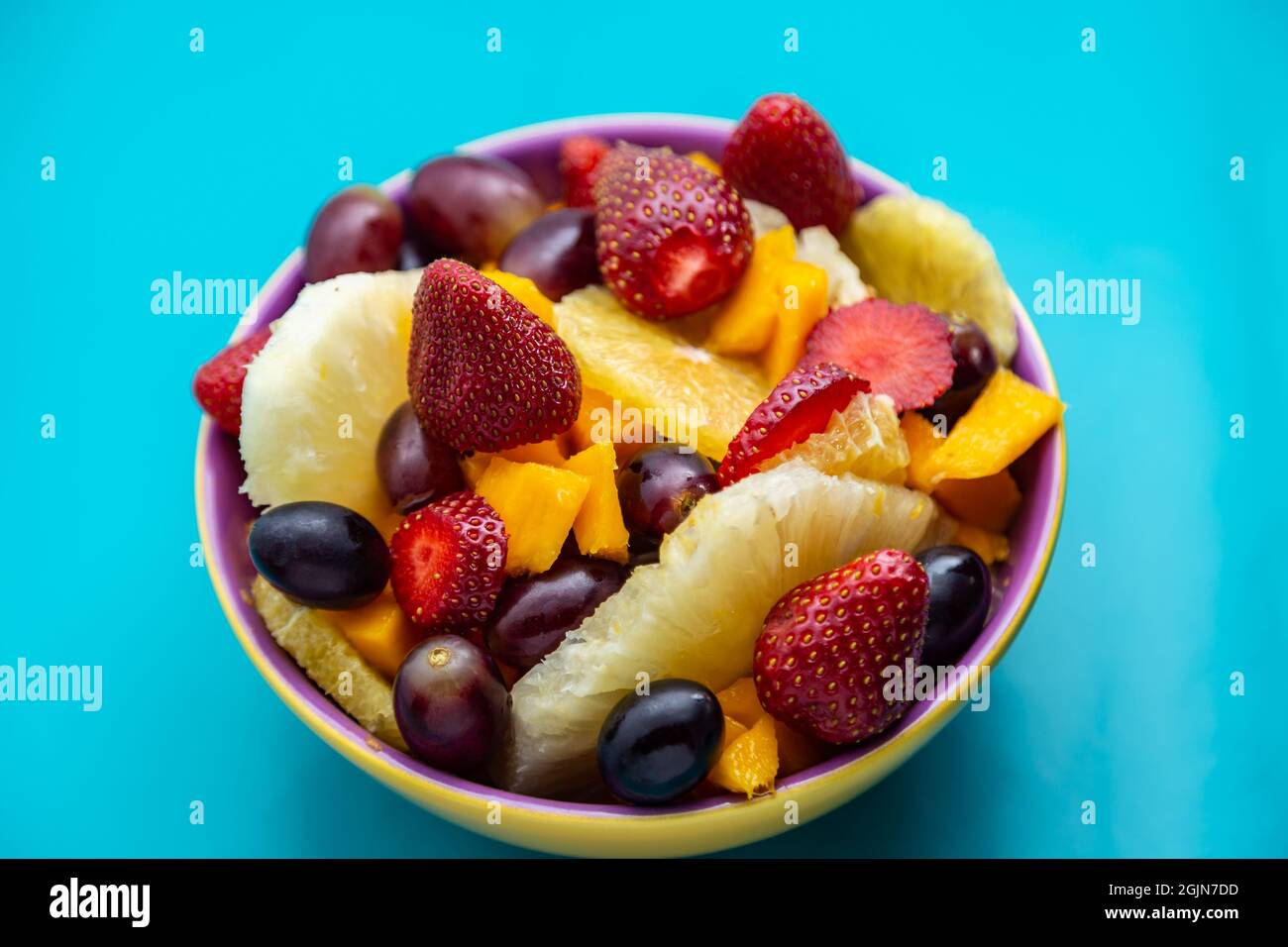 Eine Portion Obstsalat in einer gelben Schüssel mit tiffany-blauem Hintergrund. Stockfoto