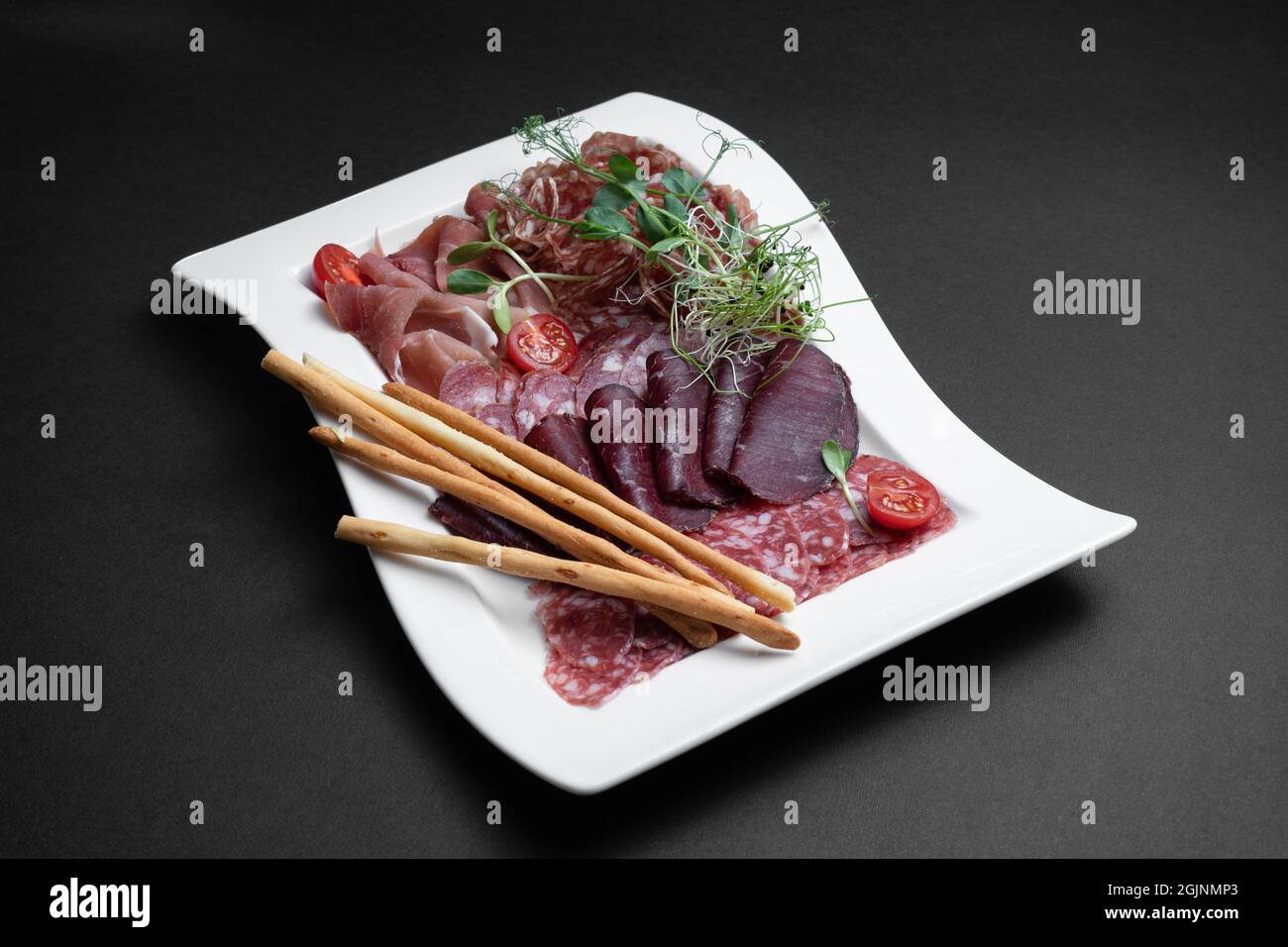 Kalte Fleischplatte mit Salami, Prosciutto und Brotstäbchen auf schwarzem Hintergrund Stockfoto