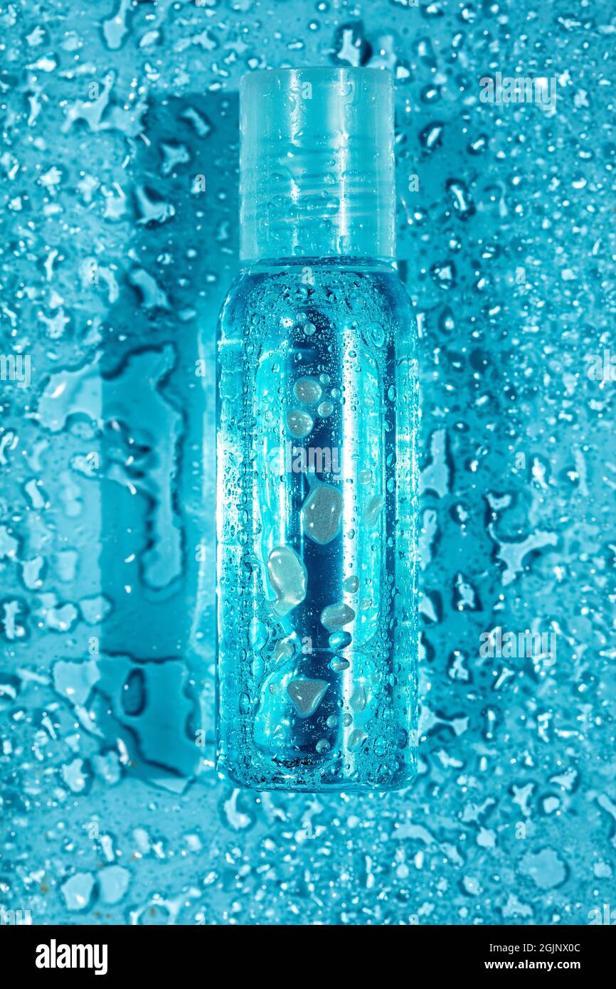 Kleine transparente Flasche mit Wassertropfen auf blauem Hintergrund, Draufsicht, vertikale Komposition Stockfoto