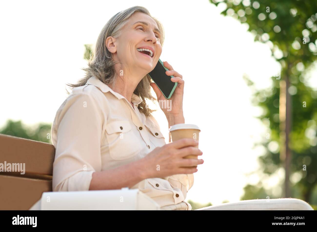 Fröhliche Frau mit Kaffee im Gespräch auf dem Smartphone Stockfoto