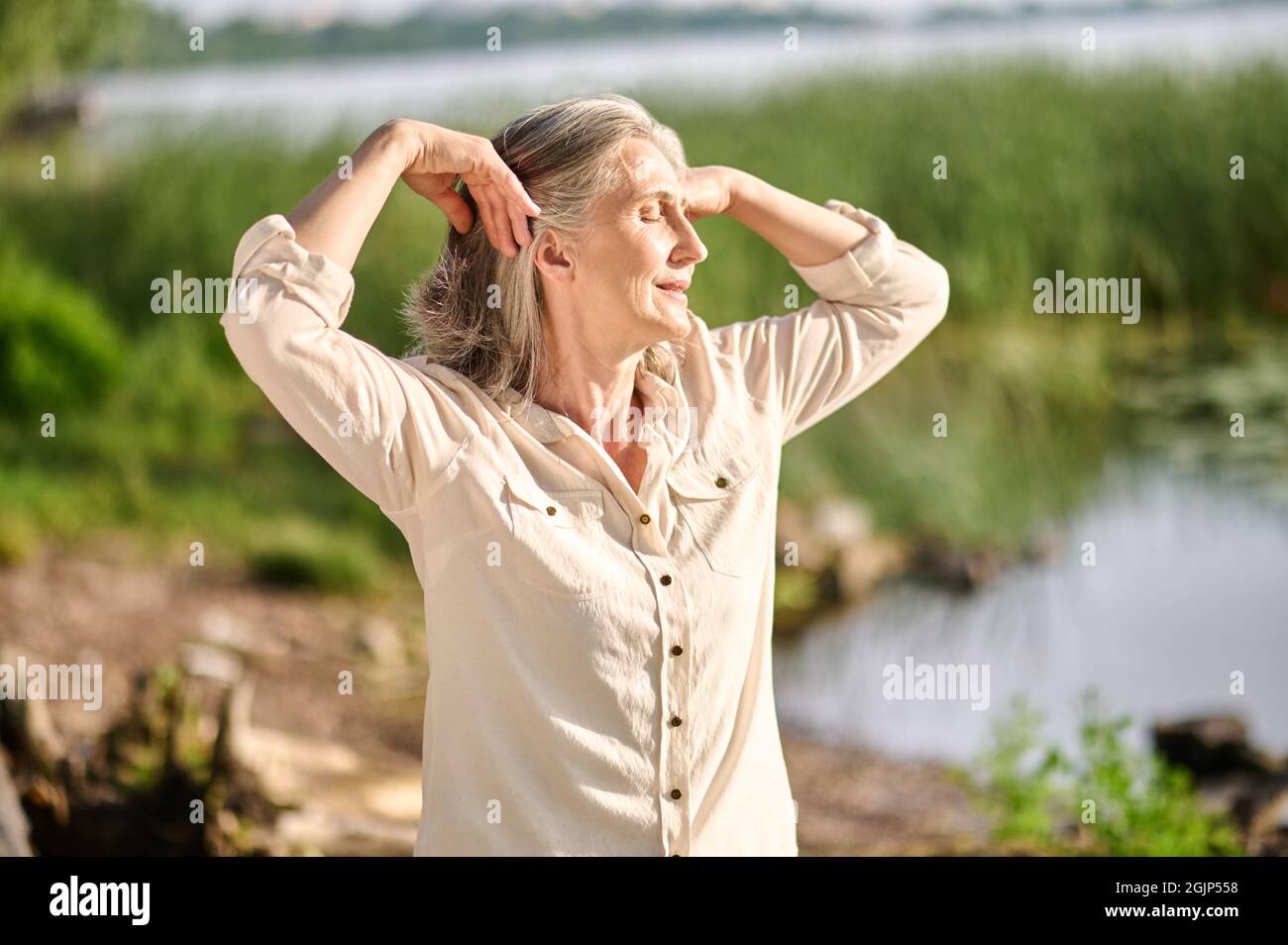 Frau mit geschlossenen Augen in der Nähe von Teich in der Natur Stockfoto