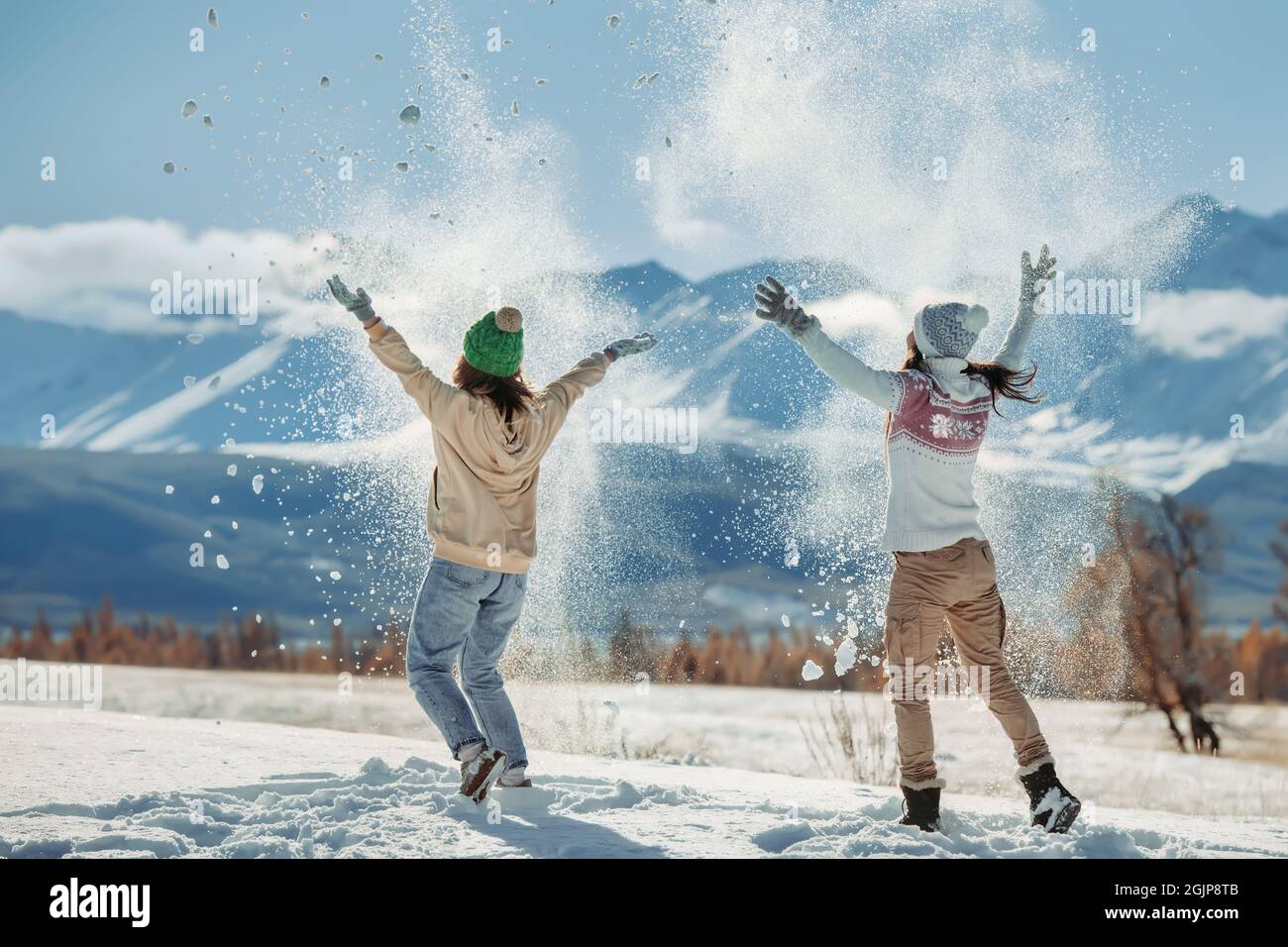 Zwei glückliche junge Mädchen haben Spaß und werfen Schnee in die Berge. Konzept für Winterferien Stockfoto