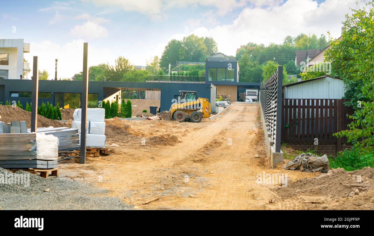 Bau eines privaten Hauses. Der Kompaktlader arbeitet auf einer Baustelle. Nivellierung des Bodens in der Landschaftsgestaltung. Vertikales Layout der Website. Stockfoto