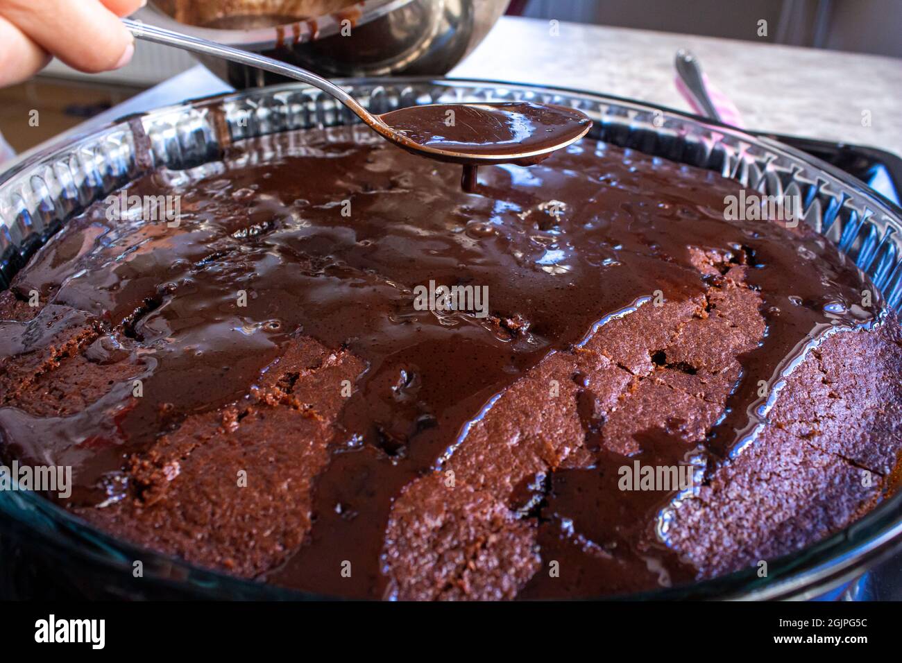 Junge Frau gießt Schokoladenpraline auf hausgemachten Kuchen. Kochen hausgemachter Desserts. Stockfoto