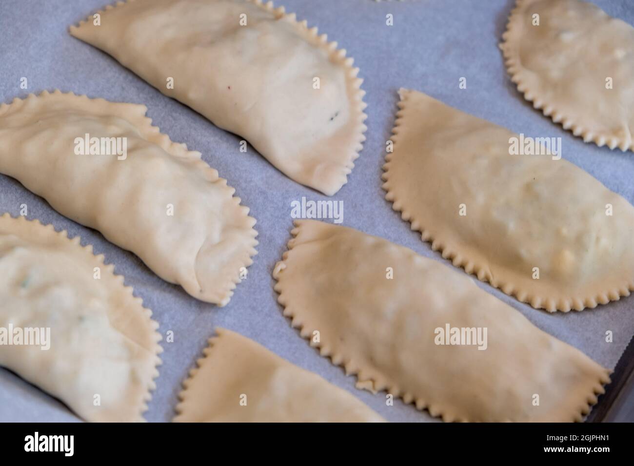 Kalitsounia ungekochte Pasteten auf Antihaftpapier zum Backen. Oben Blick auf Kaltsounia roher Teig traditionelle Lebensmittel der Insel Kreta Griechenland mit Zutaten ein Stockfoto