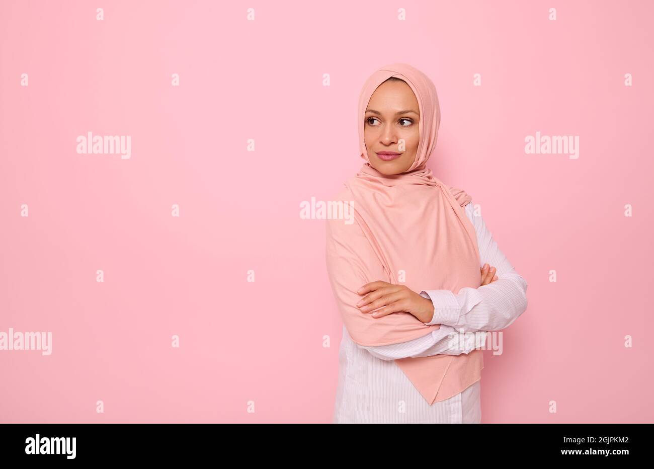 Selbstbewusstes Porträt der arabischen muslimischen wunderschöne Frau mit attraktiven Blick und bedeckt Kopf mit rosa Hijab, steht drei Viertel vor farbigem Hintergrund Stockfoto
