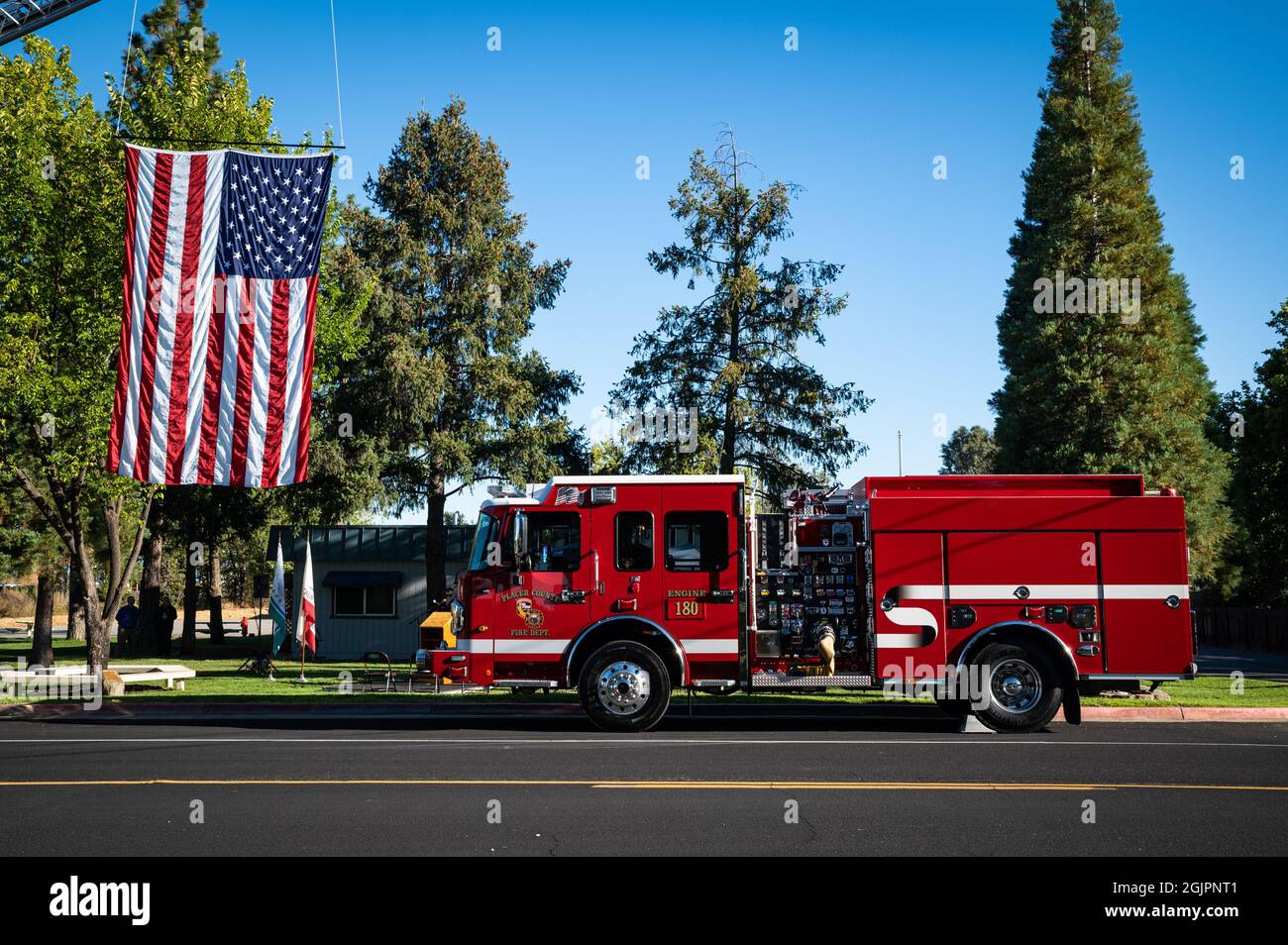 Foto eines Feuerwehrwagens und einer großen amerikanischen Flagge, die auf einer Straße im Rahmen einer Feier zum 20. Jahrestag des Bepflanzens eines Freiheitsbaums für 9/11 hängt Stockfoto