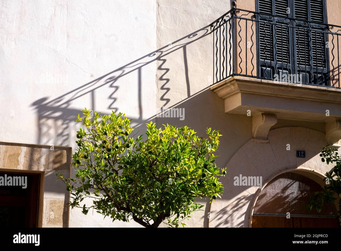Ein spärlich schmiedeeisernes Gitter wirft einen Schatten von einem Balkon auf eine Wand, Alcúdia, Mallorca, Spanien Stockfoto