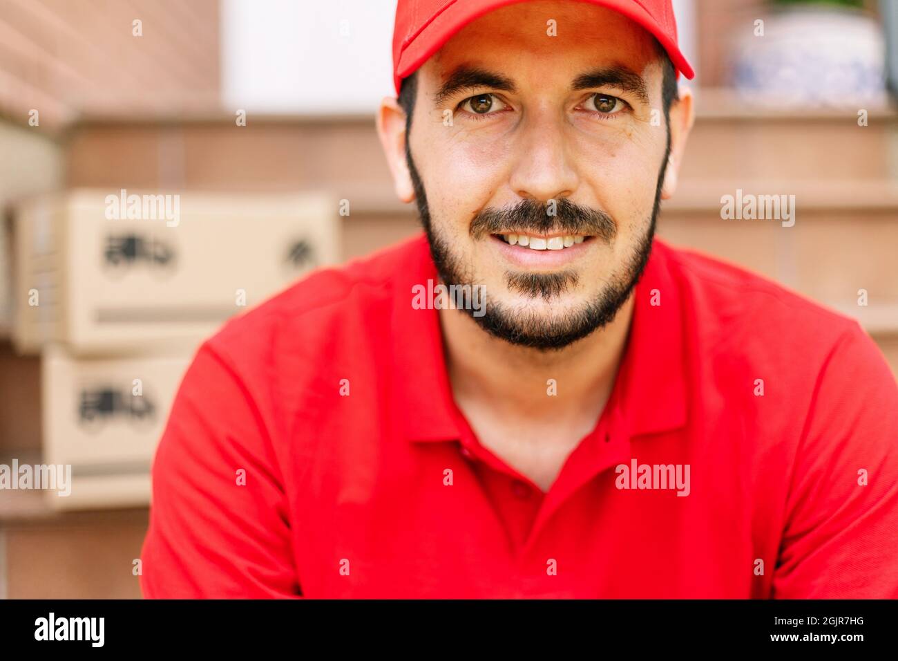 Porträt eines hispanischen Lieferers in roter Uniform mit Paketen im Hintergrund Stockfoto