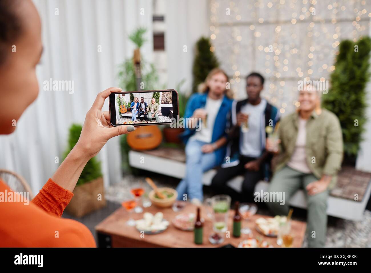 Junge Frau, die während einer Party im Freien auf dem Dach ein Smartphone-Foto von verschiedenen Gruppen junger Menschen gemacht hat Stockfoto