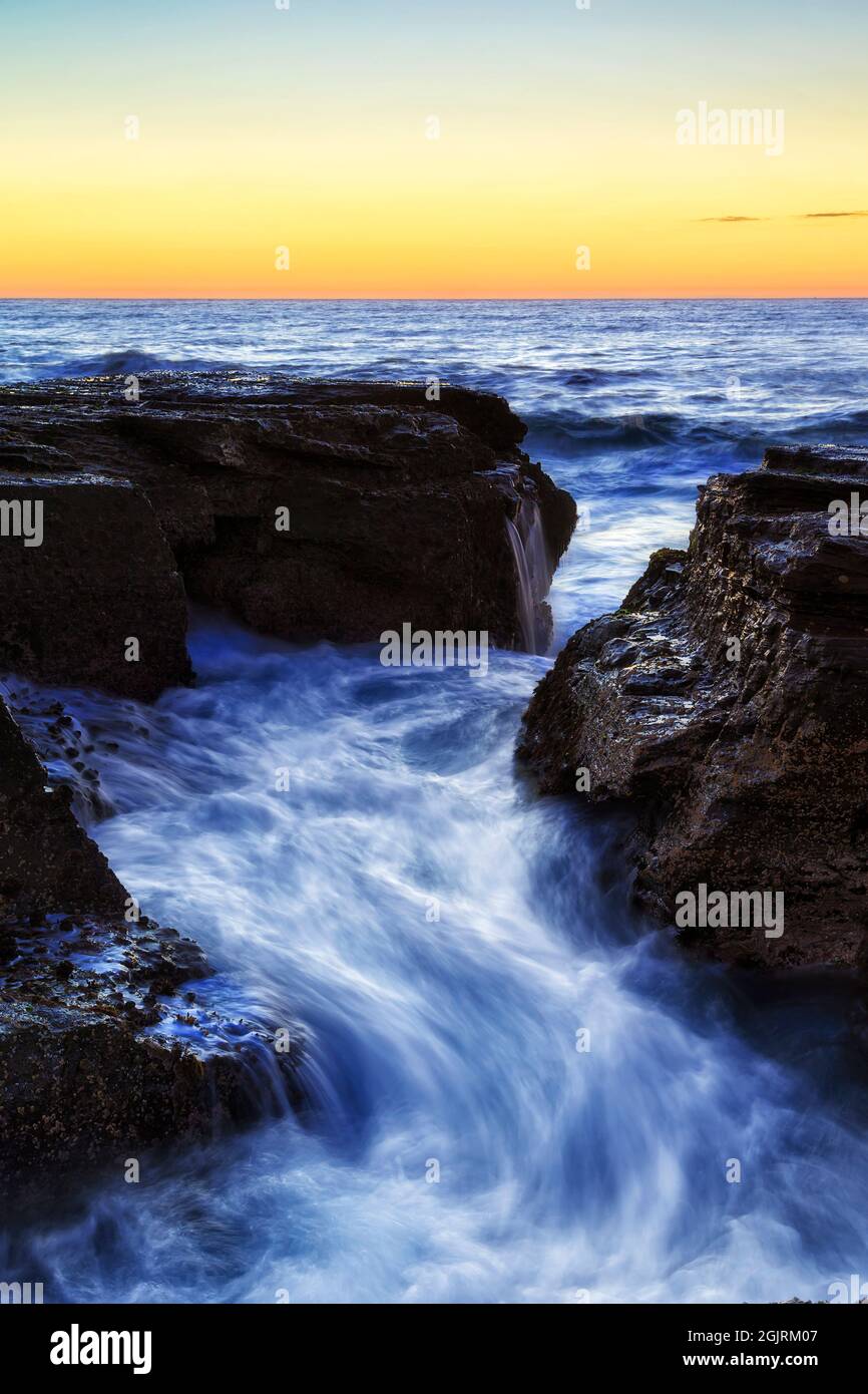 Gesprungene Sandstoenfelsen am Narrabeen-Strand an der Pazifikküste von Sydney mit malerischen Wellen bei Sonnenaufgang - Nordstrände Seeslandschaft. Stockfoto