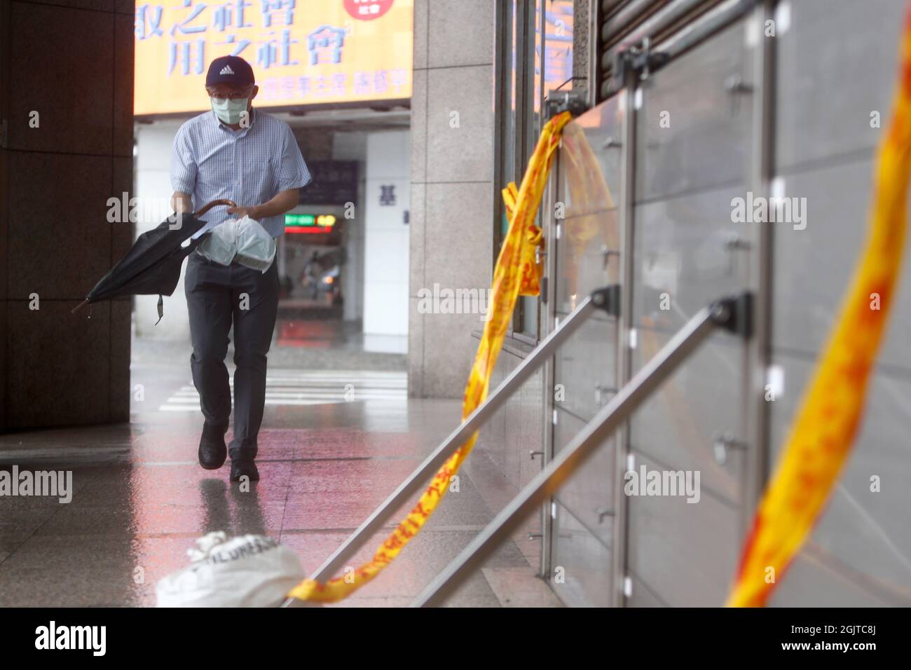 Keelung, Taipei, Taiwan. September 2021. Ein Mann mit einem Regenschirm geht an einer Blockade gegen Überschwemmungen vor einem Gebäude in Keelung vorbei, während der Taifun Chanthu, der sintflutartige Regenfälle und schädliche Winde bringt, auf der Insel landet, mit dauerhaften Auswirkungen auf China und Japan. Es wird erwartet, dass der Taifun Chantu die selbst regierte Insel mit sintflutartigen Regenfällen und anhaltenden Winden treffen wird, wobei Schulen und Unternehmen in einigen Teilen Taiwans ausgesetzt werden, um Verletzungen und Unfälle zu vermeiden. (Bild: © Daniel Ceng Shou-Yi/ZUMA Press Wire) Bild: ZUMA Press, Inc./Alamy Live News Stockfoto