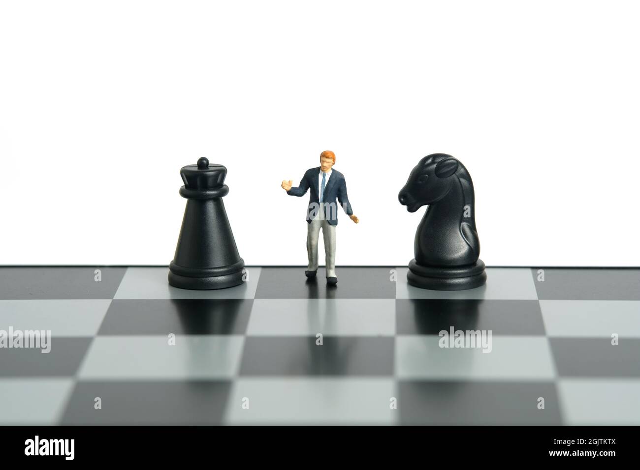 Miniatur Menschen Spielzeug Figur Fotografie. Entscheidungskonzept der Angriff- oder Verteidigungsstrategie. Ein scharfmütiger Geschäftsmann steht mit schwarzem Pferd über dem Schachbrett Stockfoto