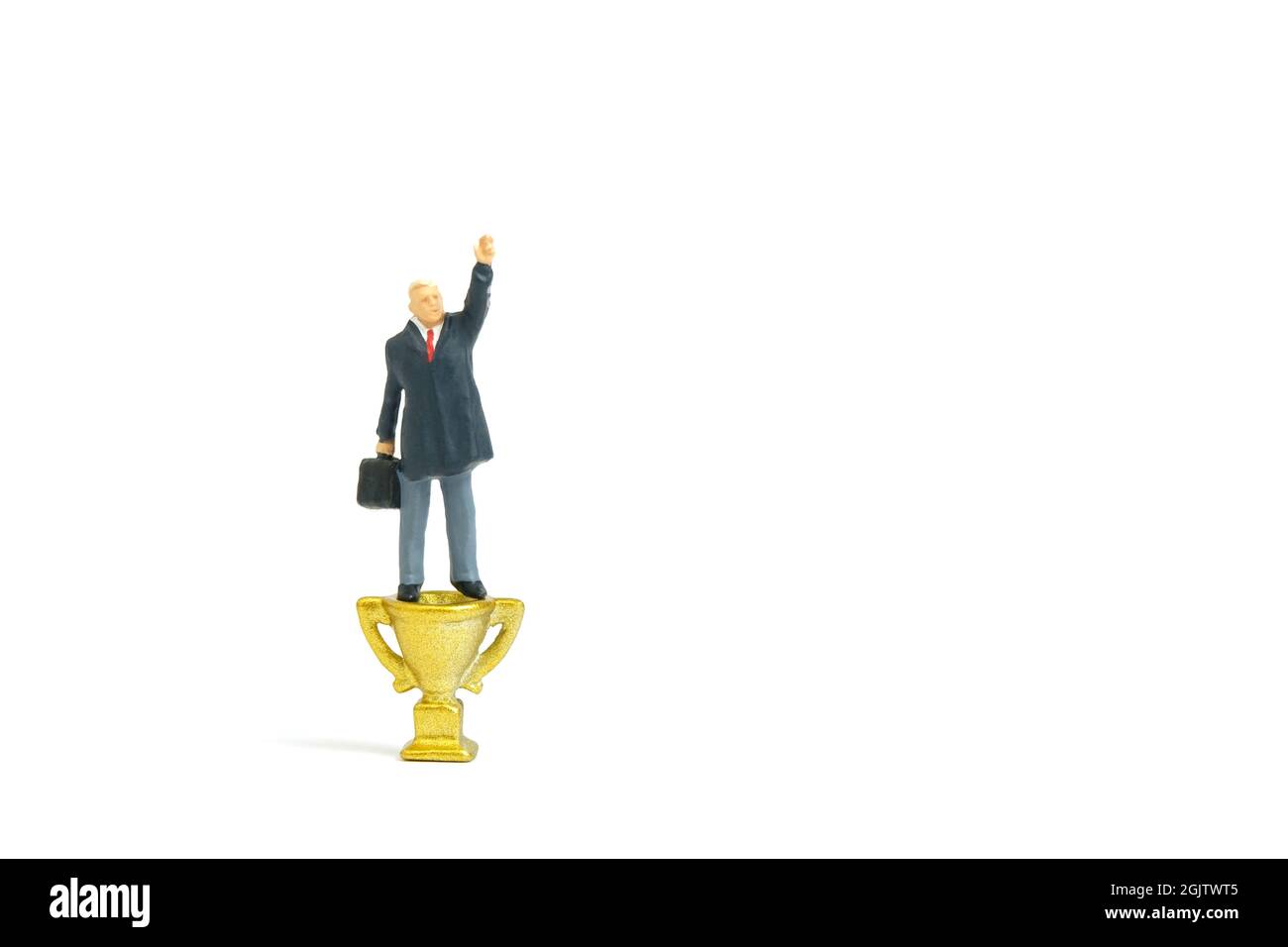 Miniatur Menschen Spielzeug Figur Fotografie. Ein Geschäftsmann, der über der Goldtrophäe steht, entscheidet, zu gewinnen oder ein Gewinner zu werden, während er seine Hand hebt. Isoliertes o Stockfoto
