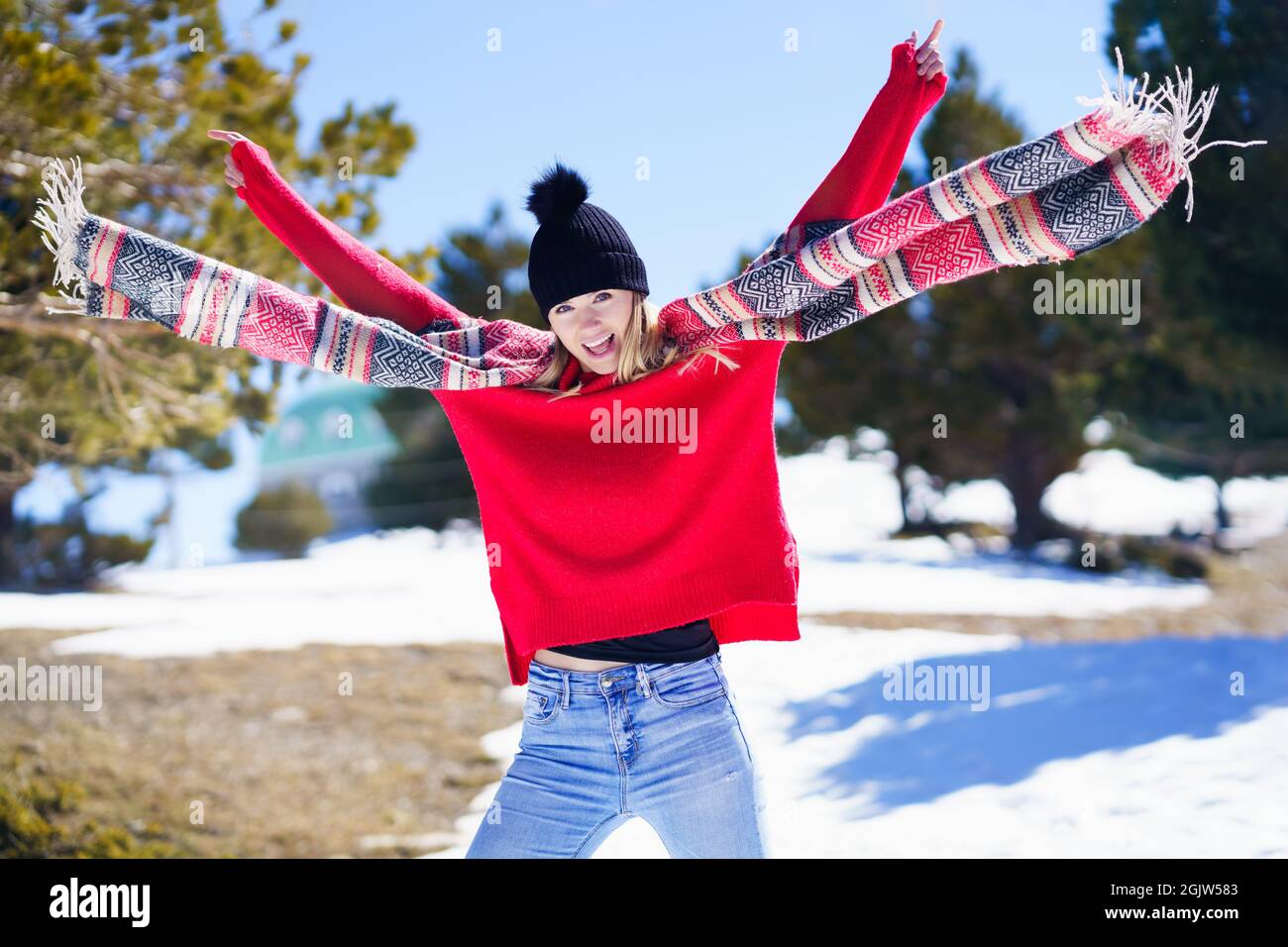 Glückliche junge blonde Frau, die ihren Schal im Wind in einem Wald in den verschneiten Bergen schwenkt. Stockfoto