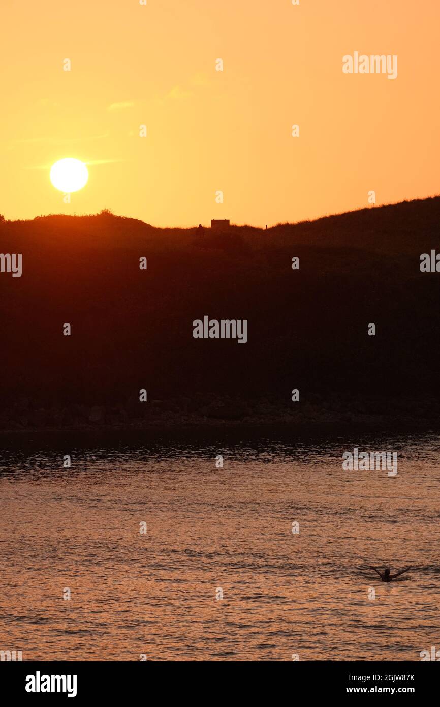 Eine alleinreisende Frau, die bei Sonnenuntergang in der Broughton Bay auf der Gower Peninsula, Wales, Großbritannien, badete Stockfoto