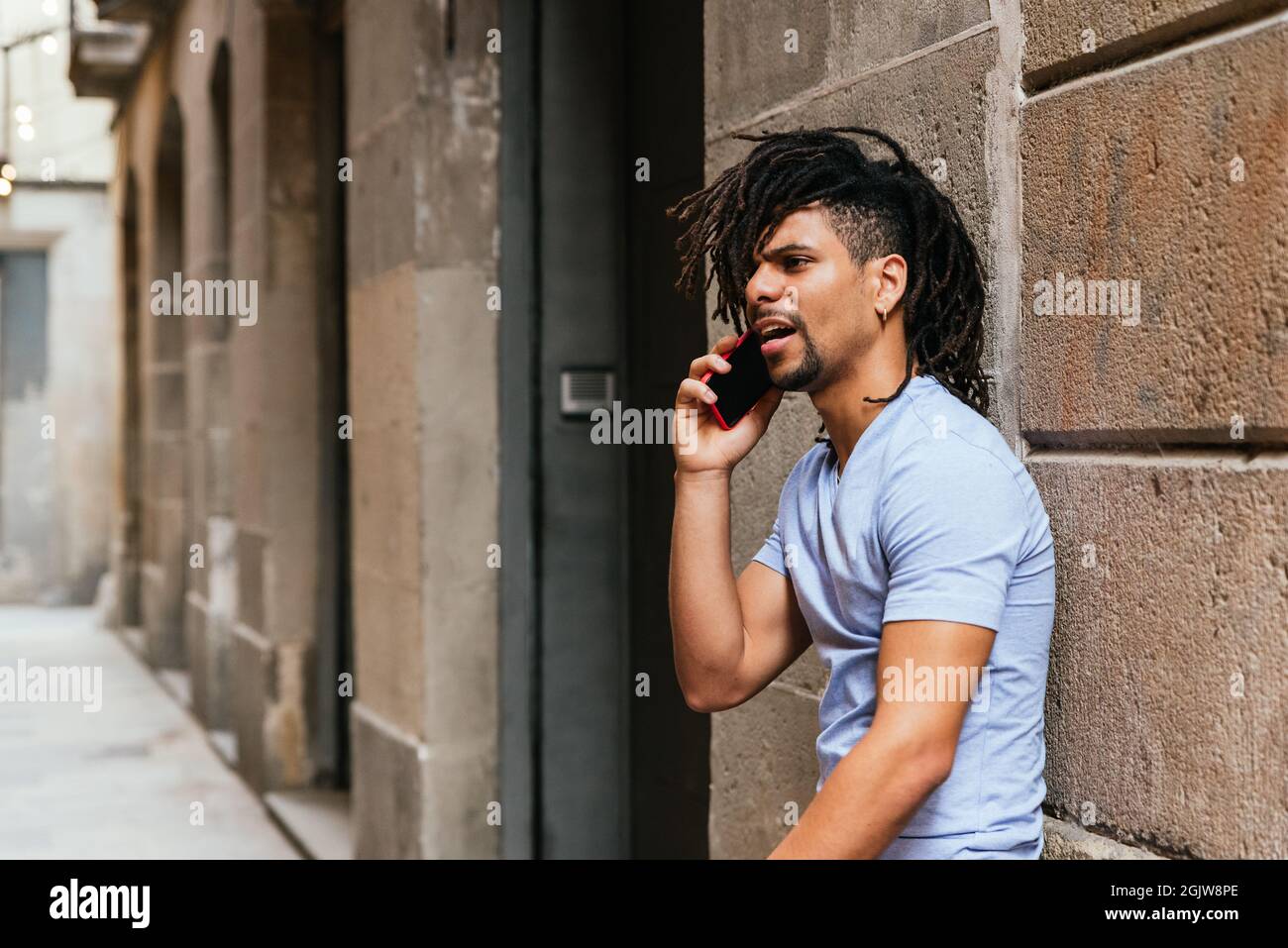 Horizontales Porträt eines lateinamerikanischen Mannes mit Dreadlocks, die per Telefon sprechen. Er ist auf der Straße und sieht wütend aus Stockfoto