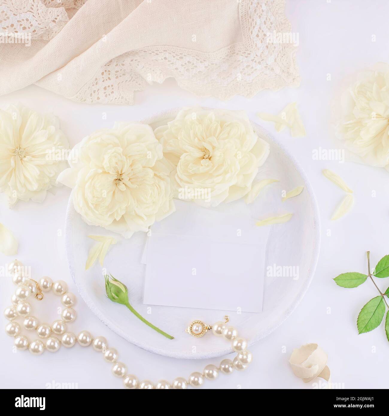 Visitenkarten mockup auf einem weißen Teller mit Rosen und Perlenkette. Einladung zur Hochzeit oder zum Geburtstag. Feminin Stockfoto