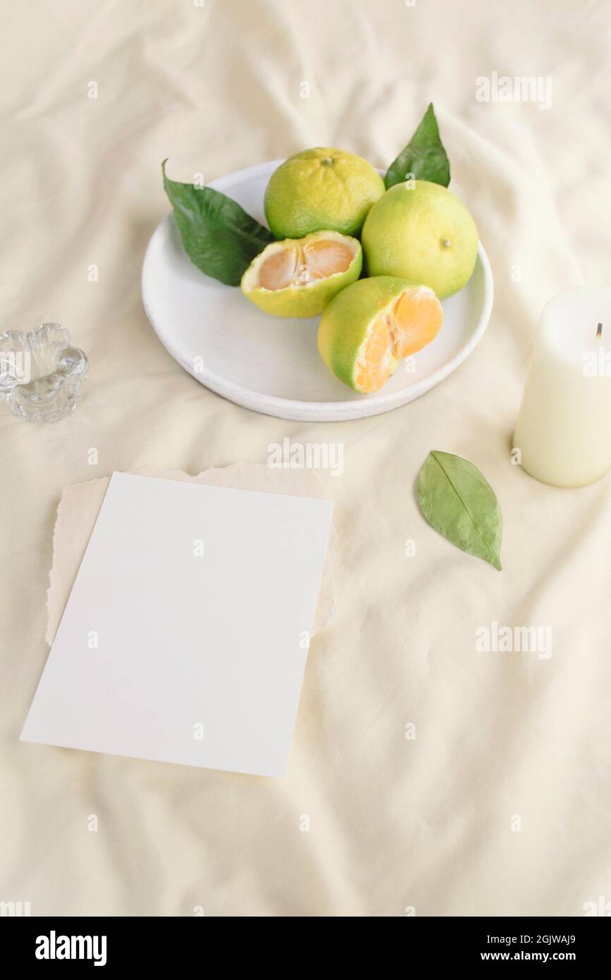 Flyer-Modell, Nachahmung einer leeren Grußkarte auf dem Bett mit einem Teller frischer Mandarinen und weißer Kerze. Morgen, Frühstück. Hochzeit, Geburtstag Stockfoto