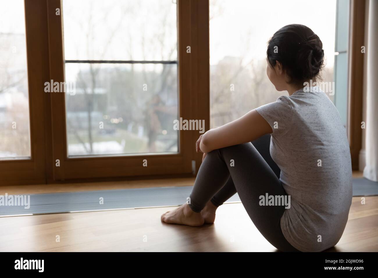 Verträumte junge Hündin in Sportswear, die sich durch ein großes Panoramafenster entspannt Stockfoto