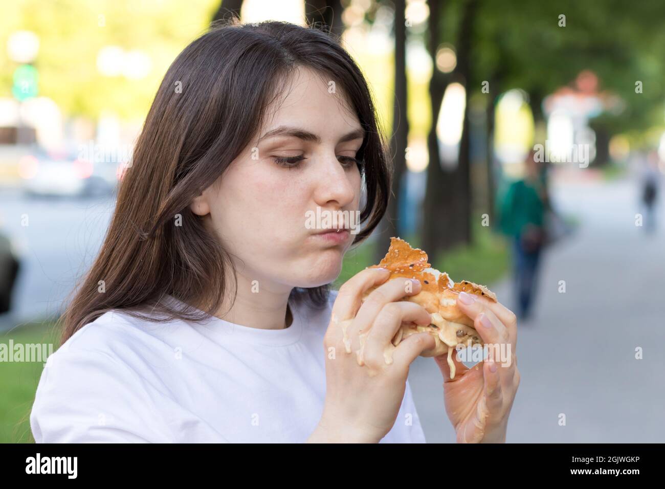 Brünette Frau überfrisst auf einem Burger auf der Straße. Völlerei, überschüssige Kalorien und Bulimie. Stockfoto