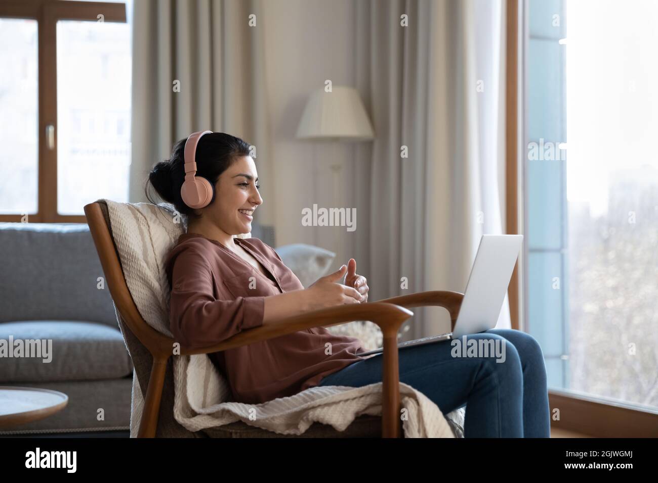 Indische Frau in Kopfhörer sitzen in bequemen Stuhl Laptop verwenden Stockfoto