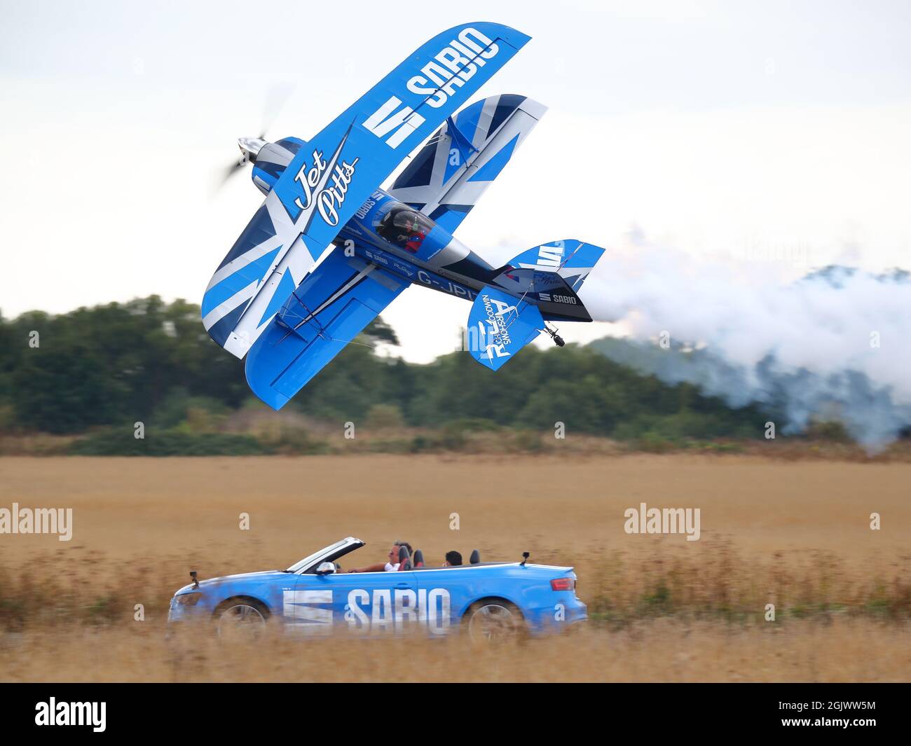 Rich Goodwin fliegt seinen blauen Pitts Special Doppeldecker G-JPIT in einem Messerkantenpass neben einem Audi-Sportwagen auf der Abingdon Air & Country Show 2021 Stockfoto