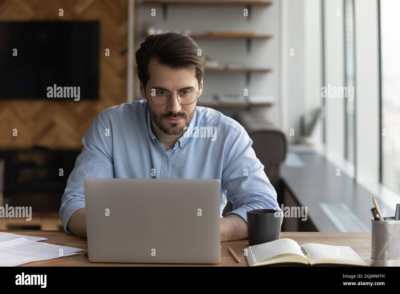 Serious Mann Blick auf Laptop-Bildschirm Arbeit online am Arbeitsplatz Stockfoto