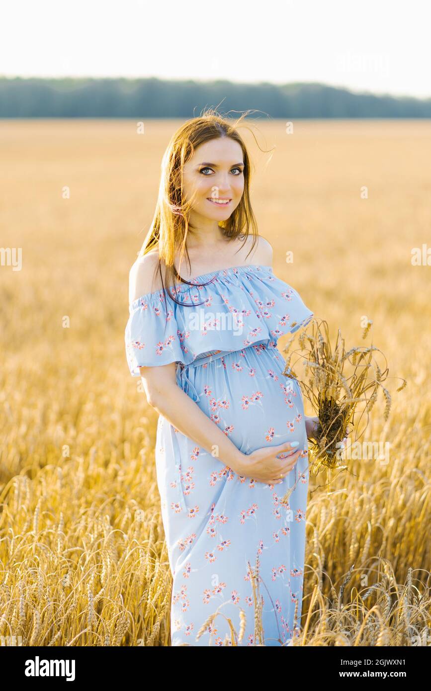 Zärtliche Schwangeren gehen auf einem Feld. Dame in blauem Kleid. Entspannen Sie sich. Die Frau wartet auf ein Baby Stockfoto