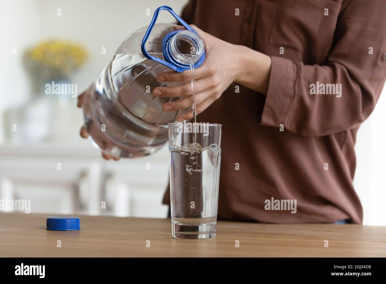 Die Hände einer jungen Frau gießen Wasser aus der Plastikflasche in das Glas Stockfoto