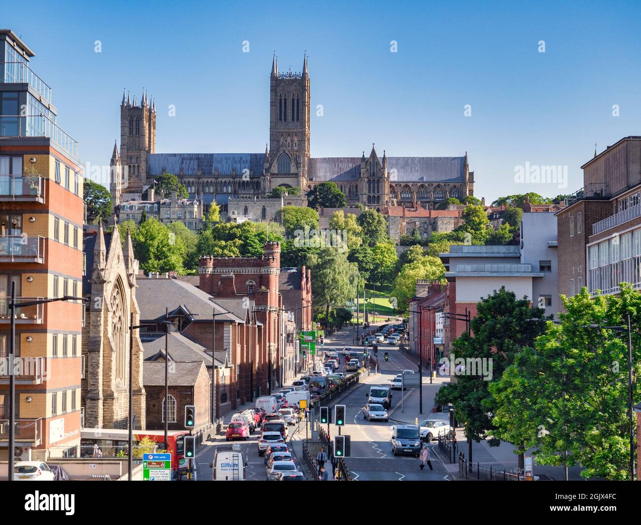 2 July 2019:Lincoln, UK - Ein Blick auf die Kathedrale, entlang Broadgate, eine geschäftige Innenstadt Straße voller Verkehr., mit klarem blauen Himmel und Bäumen in vollem Umfang Stockfoto