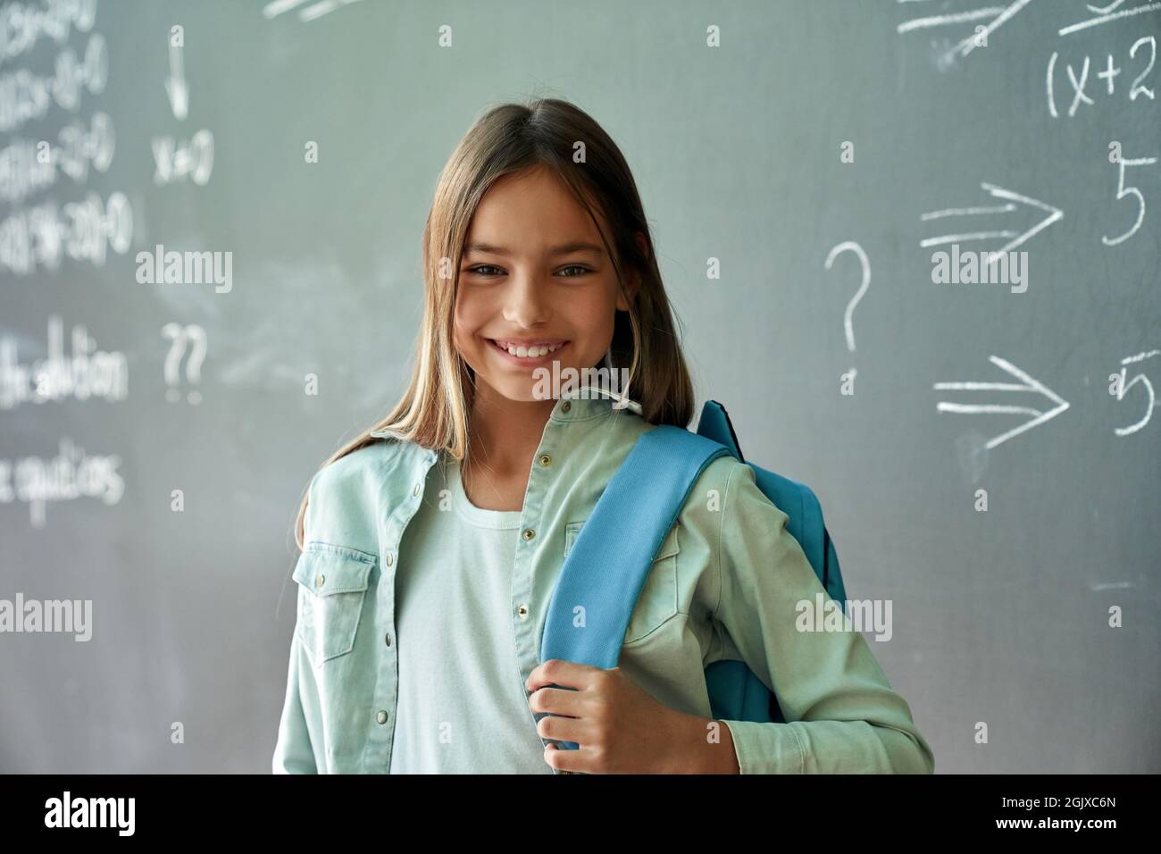 Porträt eines glücklichen lächelnden hispanischen Mädchens, das auf einem schwarzen Brett auf dem Hintergrund steht. Stockfoto