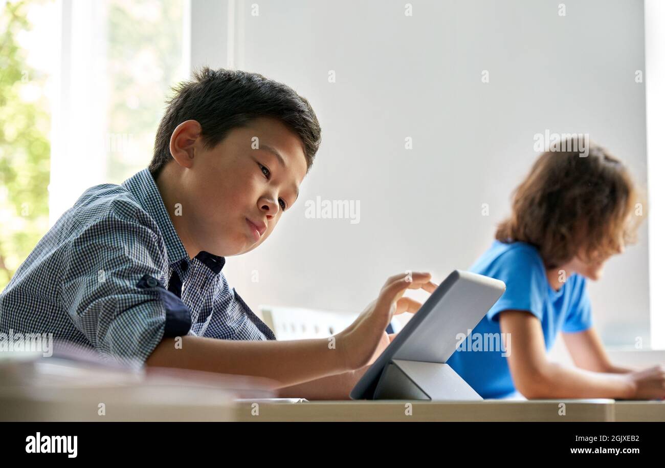 Konzentrierter asiatischer Schuljunge mit Tablet-Computer-Gerät im Klassenzimmer. Stockfoto