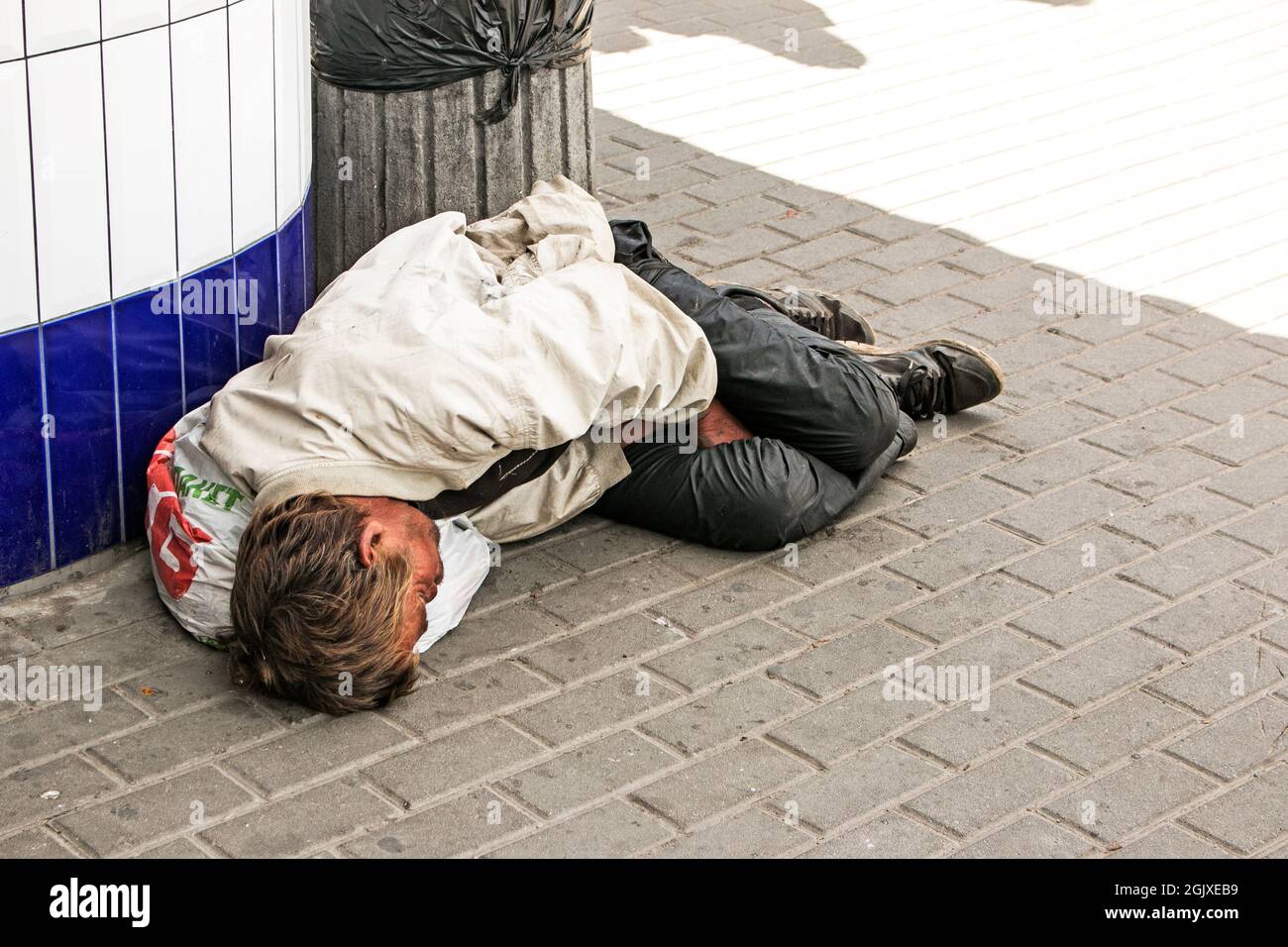 Dnepropetrovsk, UKRAINE - 09.05.2021: Ein obdachloser Bettler schläft auf der Straße. Obdachlose, schmutzige Menschen schlafen auf den gepflasterten Straßen. Soziale Probleme. Begga Stockfoto