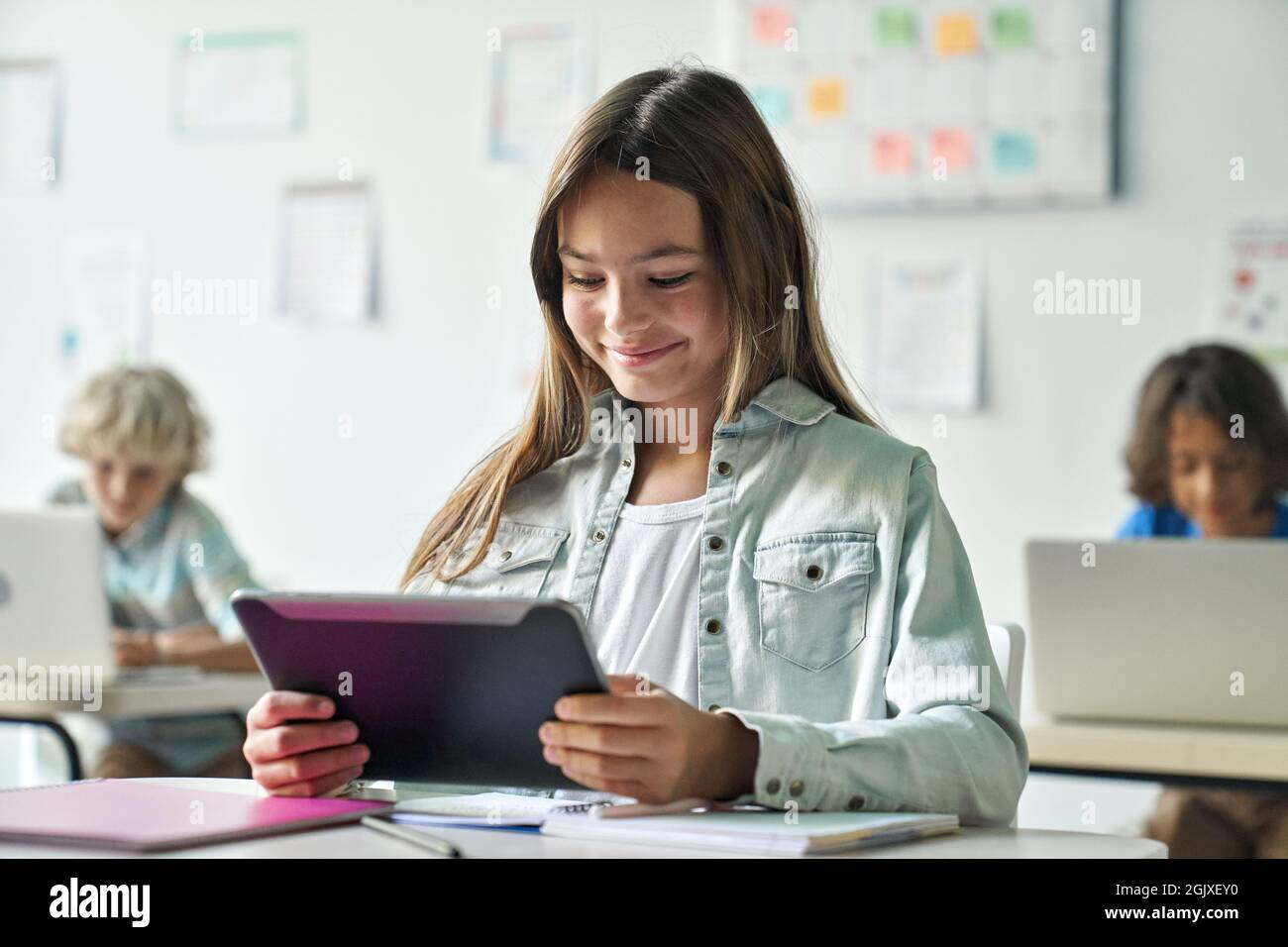 Glücklich lächelnd Schulmädchen Leseaufgabe von Tablet-Computer-Gerät im Klassenzimmer. Stockfoto