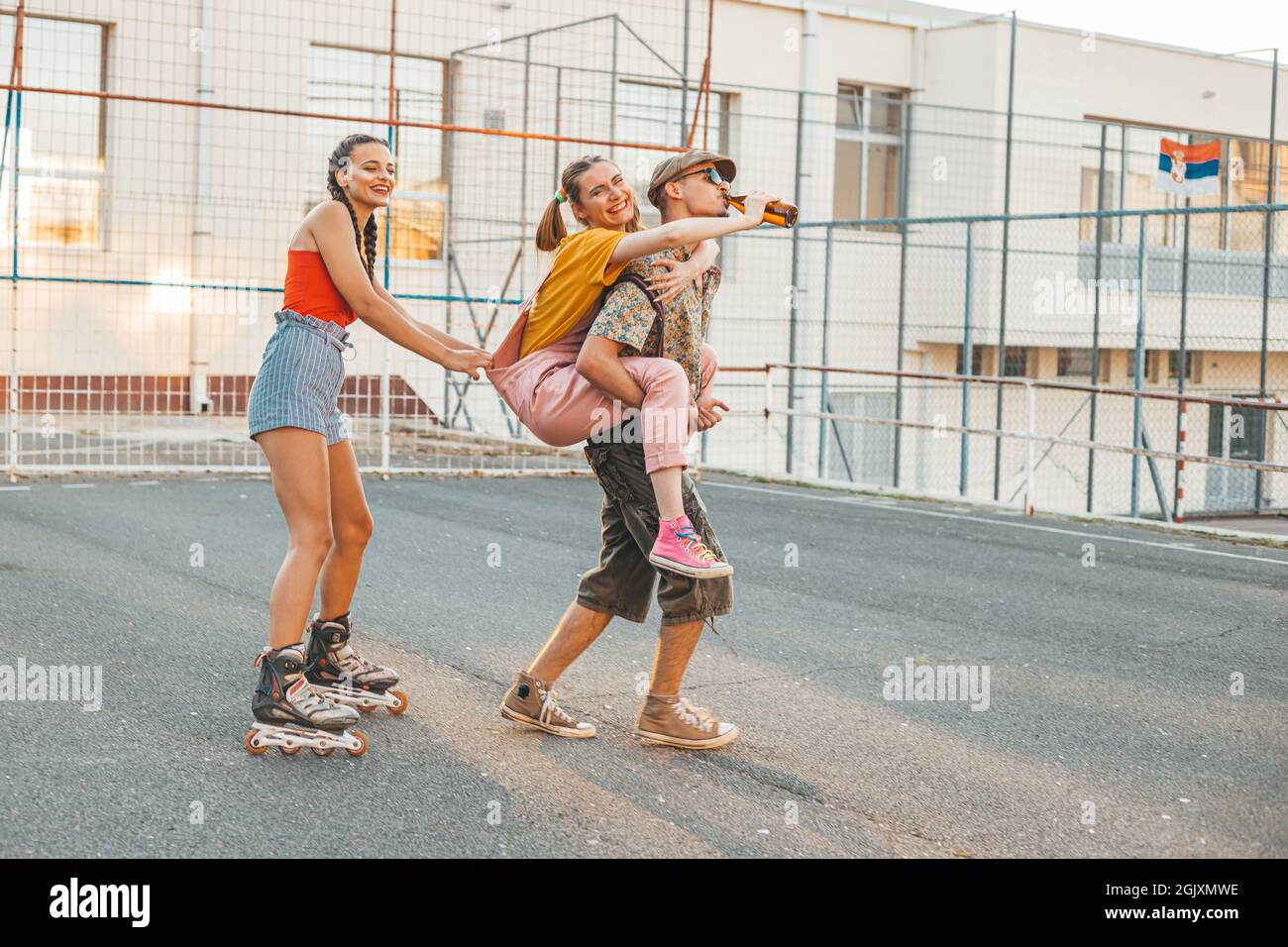 Eine Gruppe von Freunden, die draußen rumhängen. Ein Mädchen reitet zurück ihre Freundin, andere reitet hinter auf Rollen. Positive Vibes Stockfoto