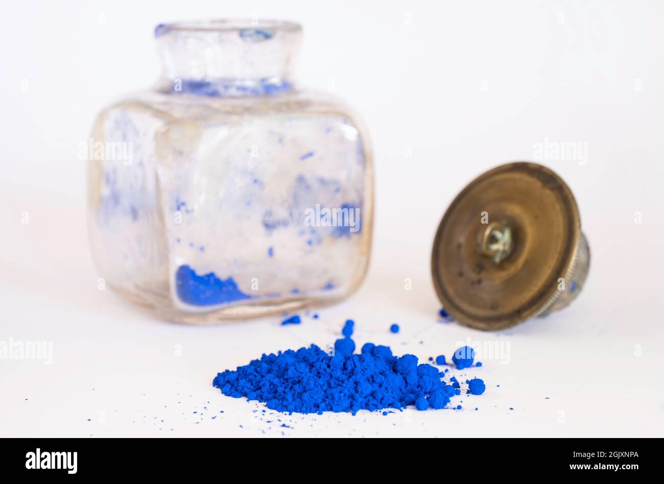 Blaues Pigment mit verschwommenem antikem quadratischem Glasfläschchen mit Kupferstopfen im Hintergrund. Das Pigment wird mit Leinöl gemischt, um Ölfarbe zu erhalten Stockfoto