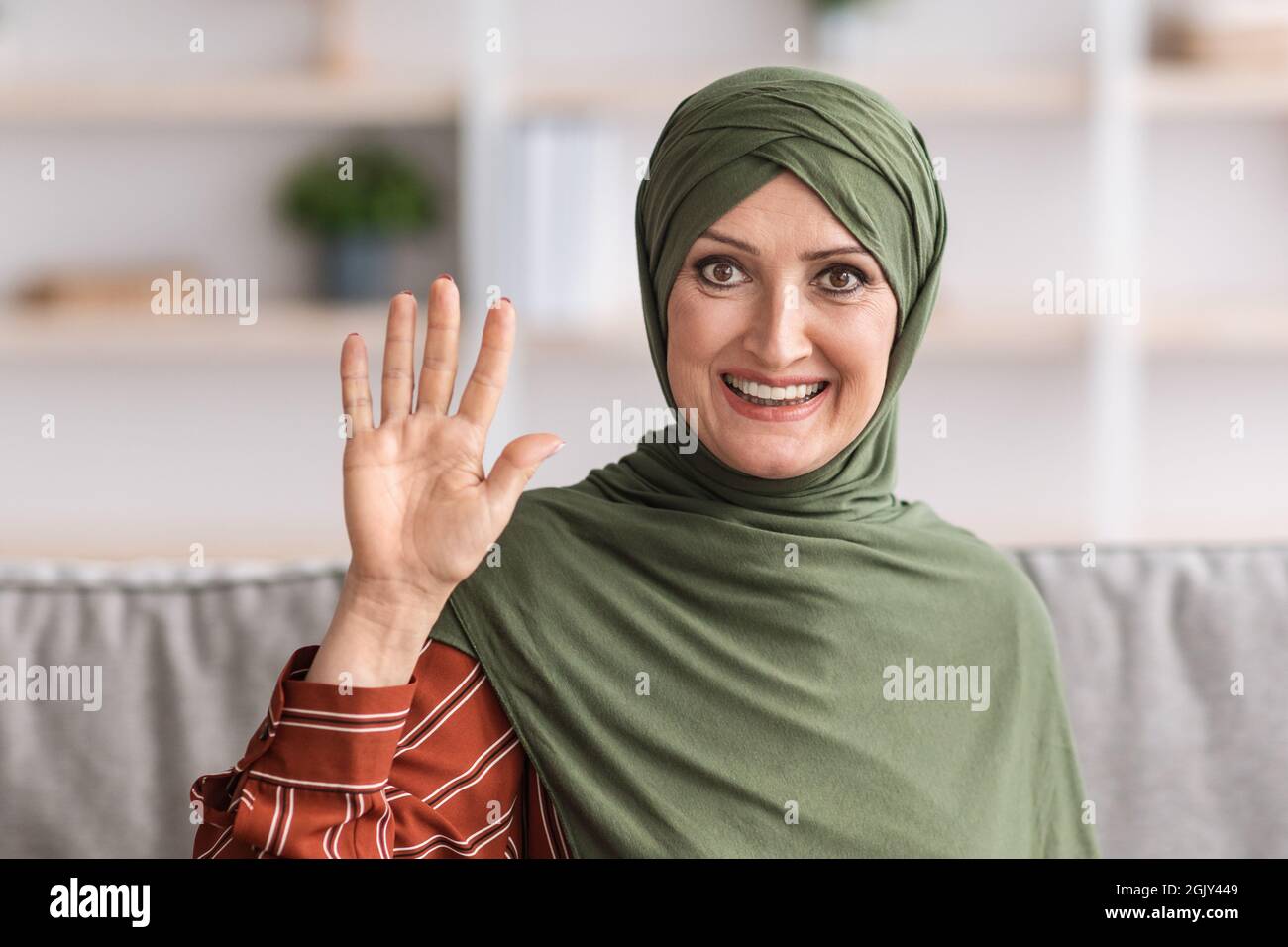 Porträt Einer Älteren Muslimischen Frau Mit Winkender Hand, Die Drinnen Sitzt Stockfoto