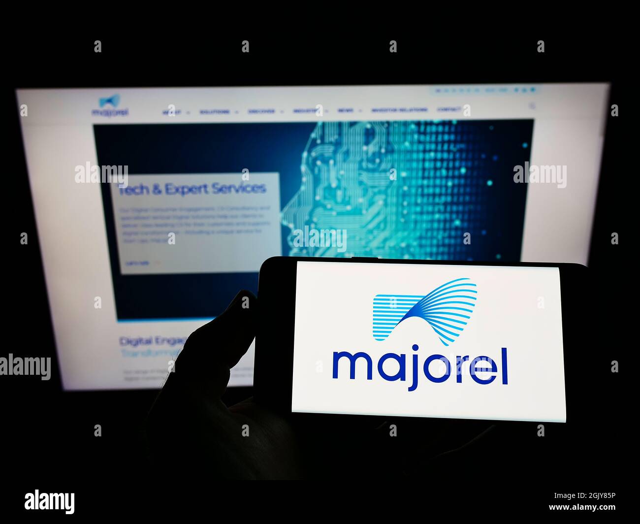 Person, die das Mobiltelefon mit dem Logo des Dienstleistungsunternehmens Majorel Group Luxembourg S.A. auf dem Bildschirm vor der Webseite hält. Konzentrieren Sie sich auf die Telefonanzeige. Stockfoto