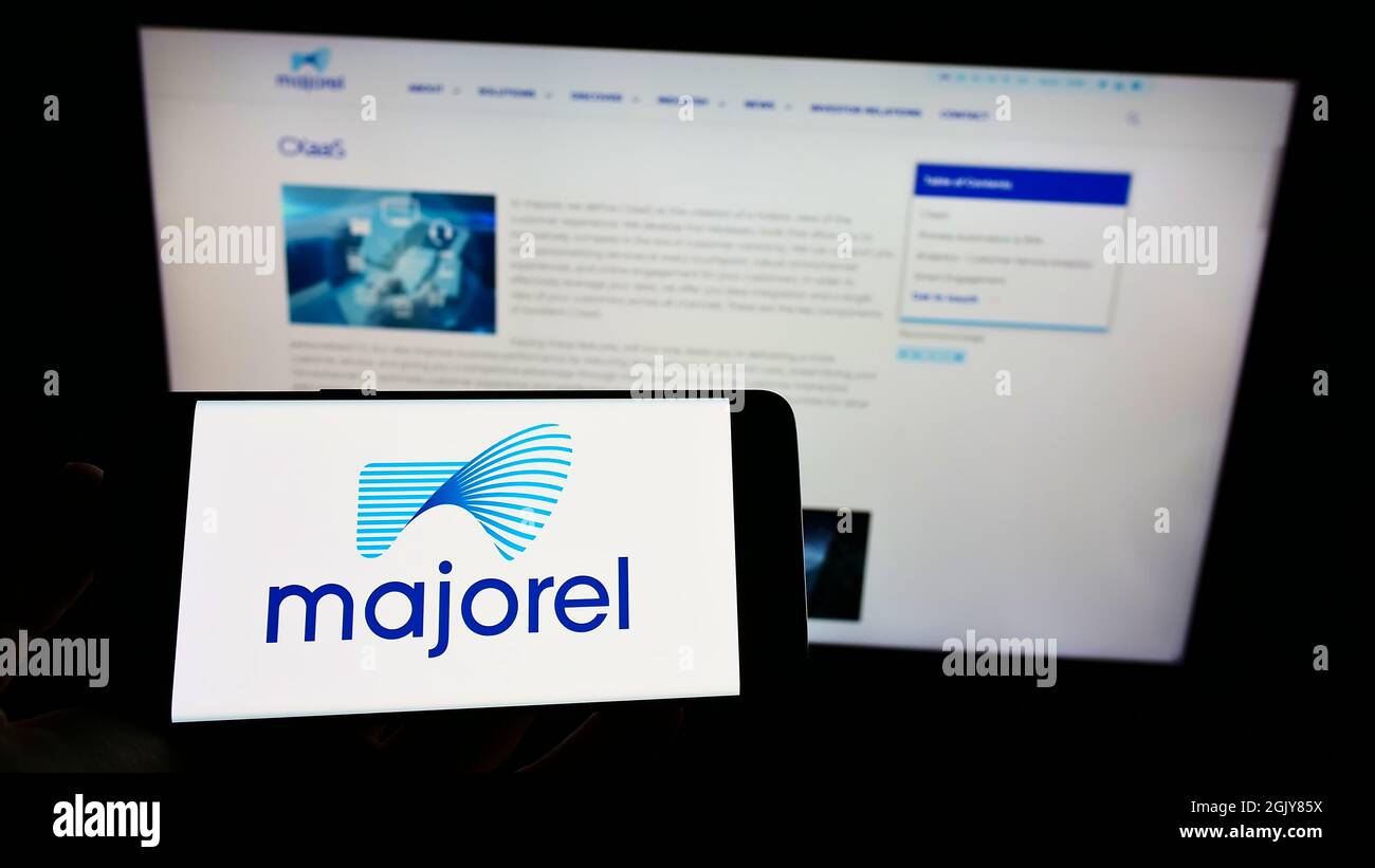 Person, die Mobiltelefon mit dem Logo des Dienstleistungsunternehmens Majorel Group Luxembourg S.A. auf dem Bildschirm vor der Geschäftswebseite hält. Konzentrieren Sie sich auf die Telefonanzeige. Stockfoto